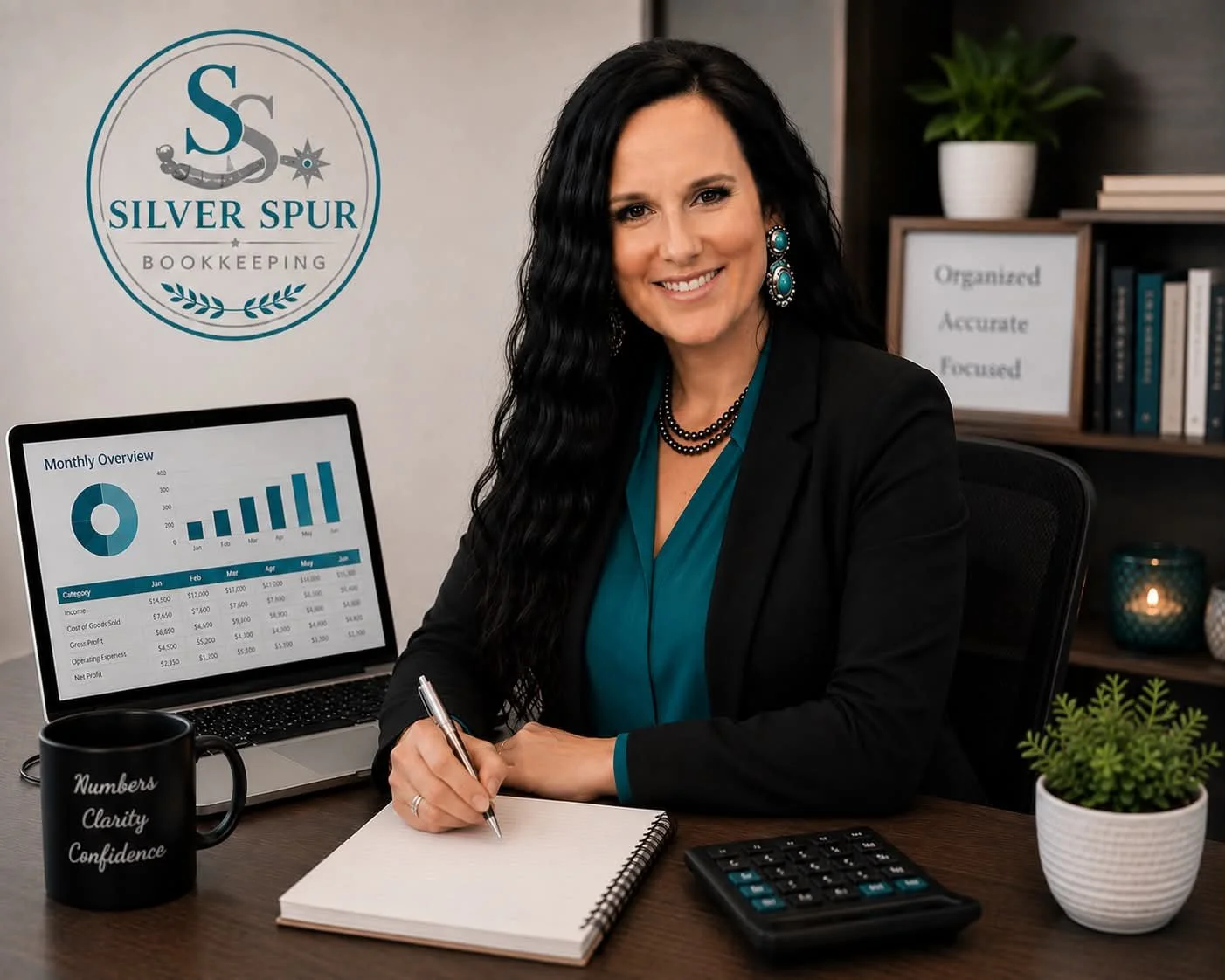 A woman with long black hair, wearing turquoise earrings and a matching blouse under a black blazer, sitting at a desk with a laptop displaying a monthly overview graph, a notebook, a black mug with the words "Numbers Clarity Confidence," a calculator, and a potted plant. Behind her is a bookshelf with a framed sign that reads "Organized Accurate Focused" and a white pot with a green plant. The logo for Silver Spur Bookkeeping is on the wall behind her.