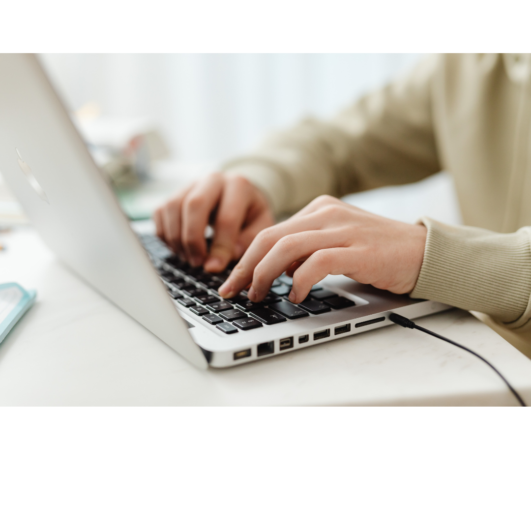 Person typing on a silver MacBook laptop with a black keyboard, sitting at a white desk.