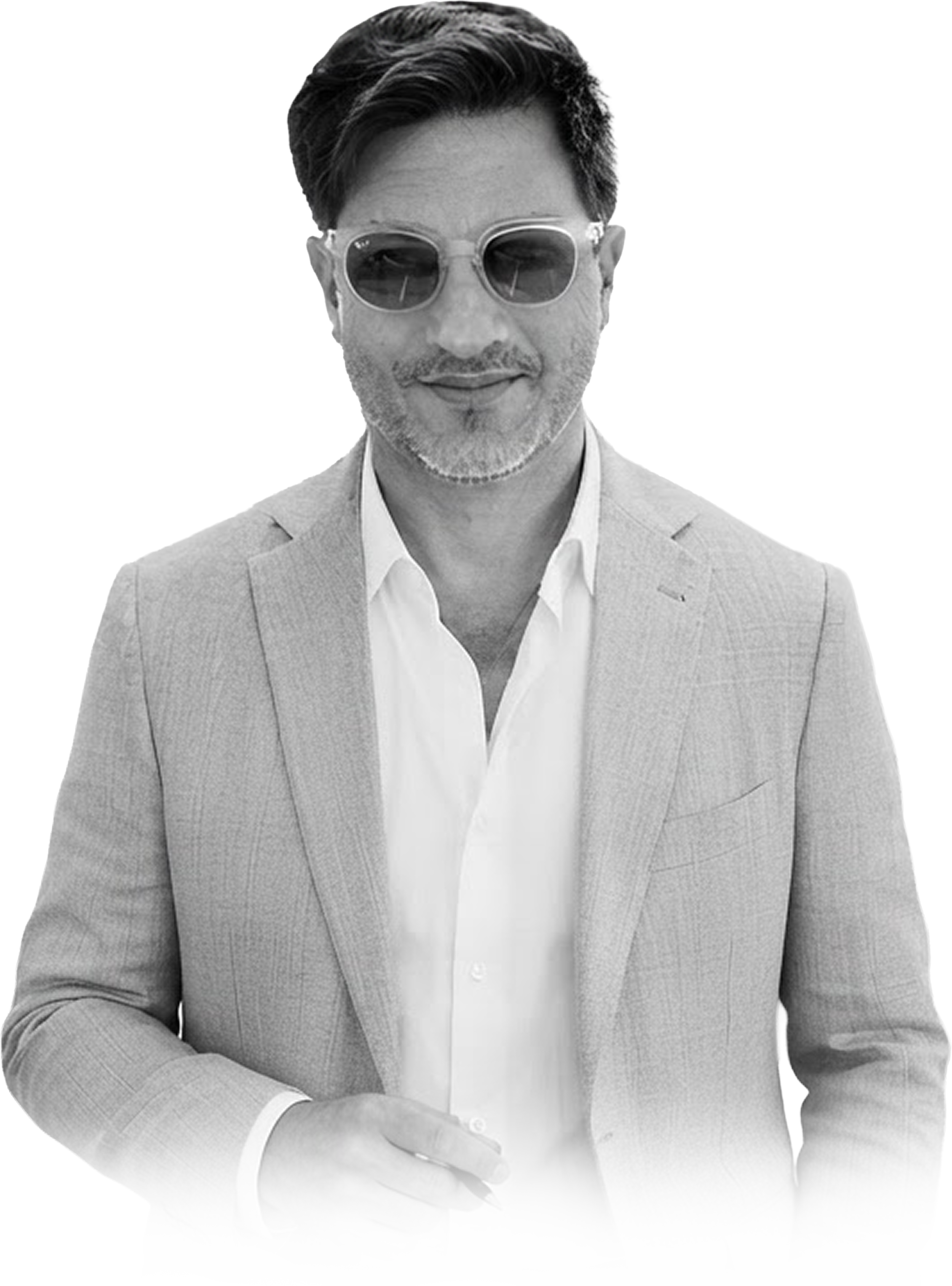 Black and white portrait of a man in a light-colored suit jacket and white shirt, wearing sunglasses, with a neatly groomed beard and stylish hair. He is holding a pen in his right hand and appears to be smiling.