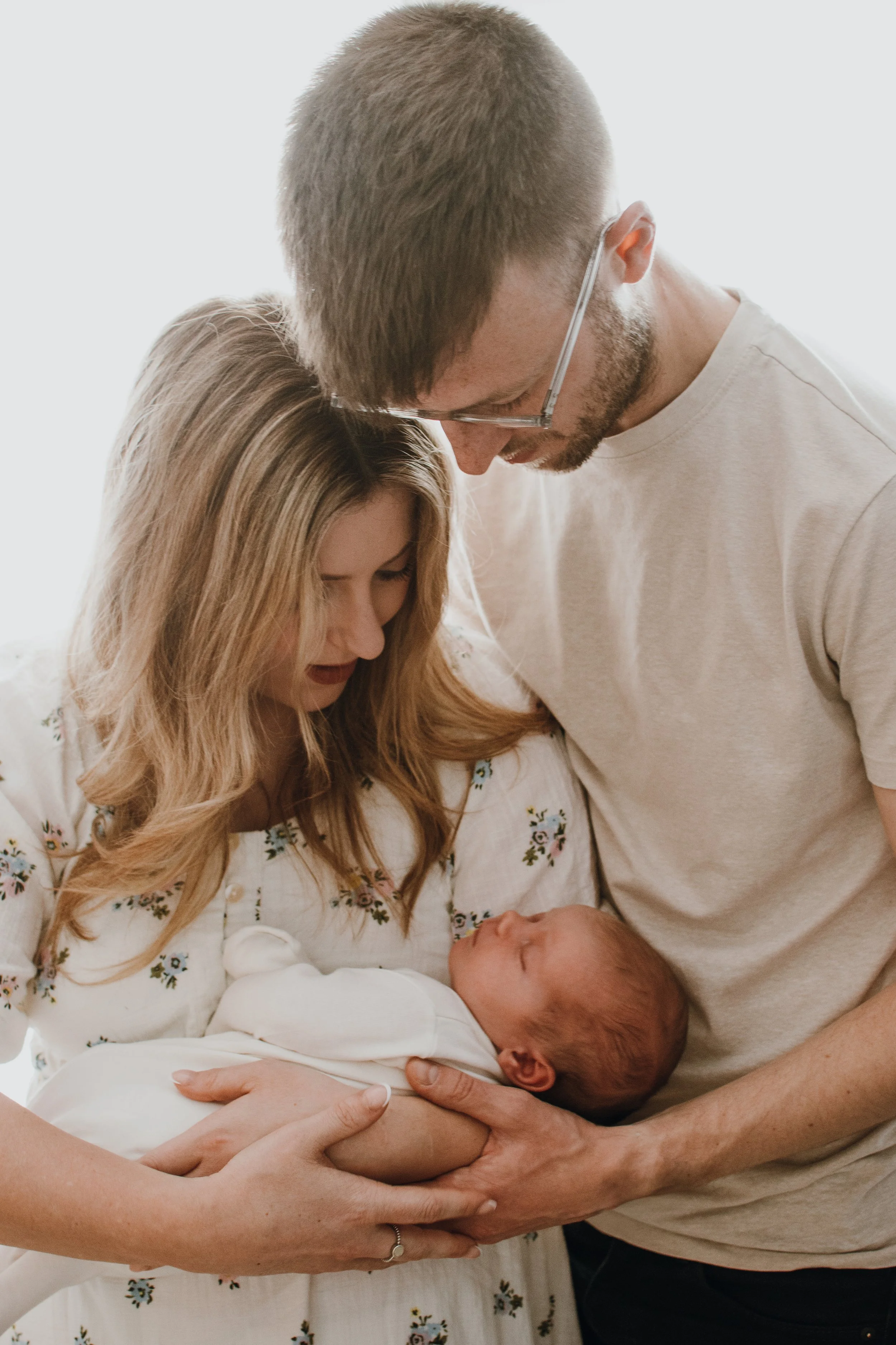 A woman is holding a newborn baby in her arms, while a man is leaning over them, both of them looking gently at the baby.