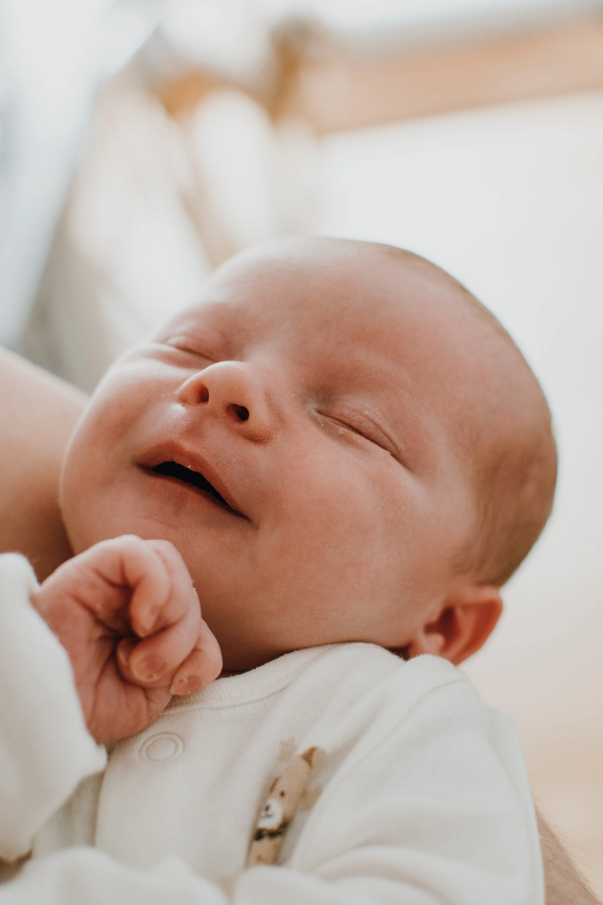 Close-up of a sleeping newborn baby wrapped in a white blanket, with soft natural lighting.