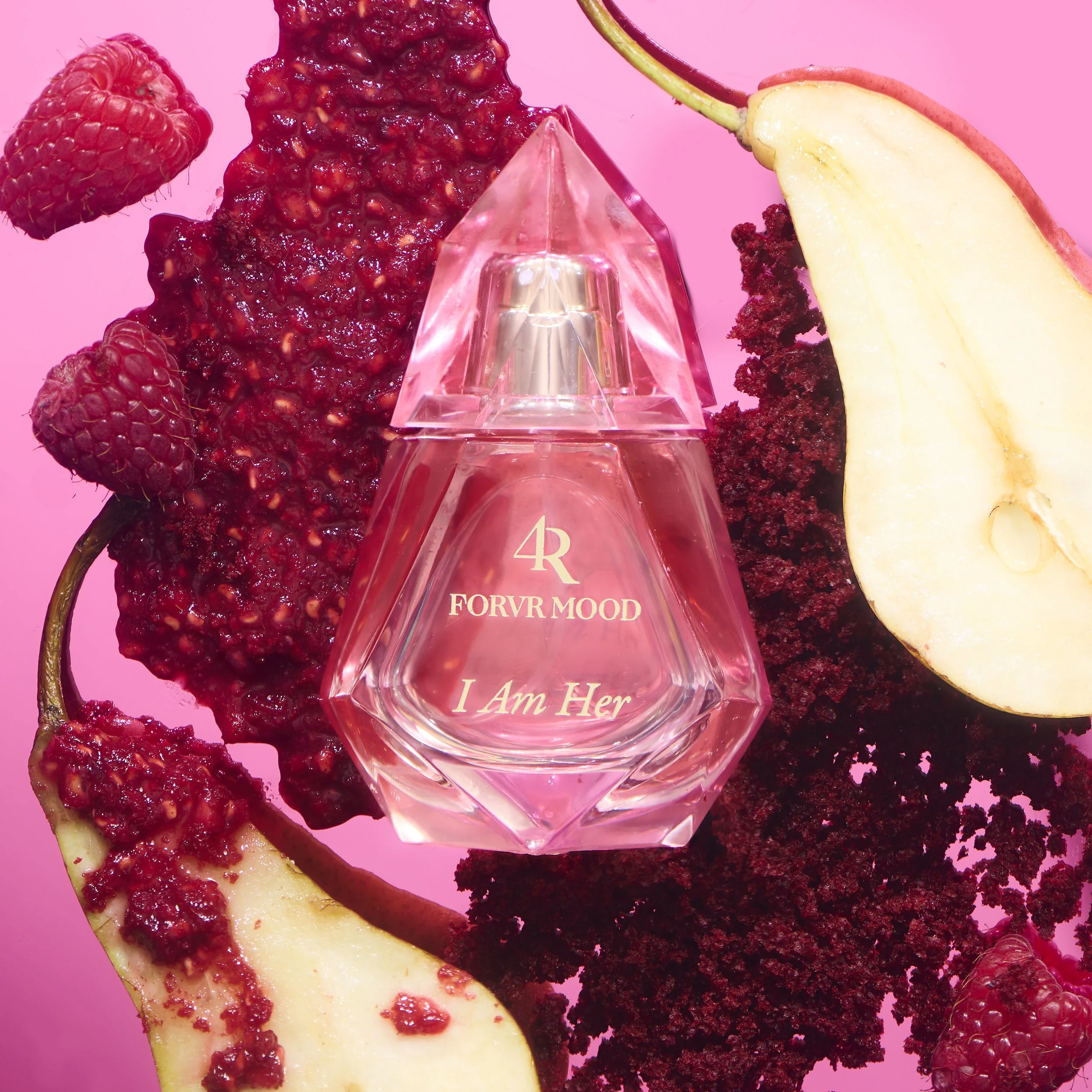 Close-up of a perfume bottle labeled 'I Am Her' surrounded by fresh raspberries, a slice of pear, and raspberry jam on a pink background.