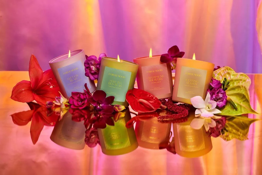 Four candles in pastel colors with floral decorations and reflected on a shiny surface.