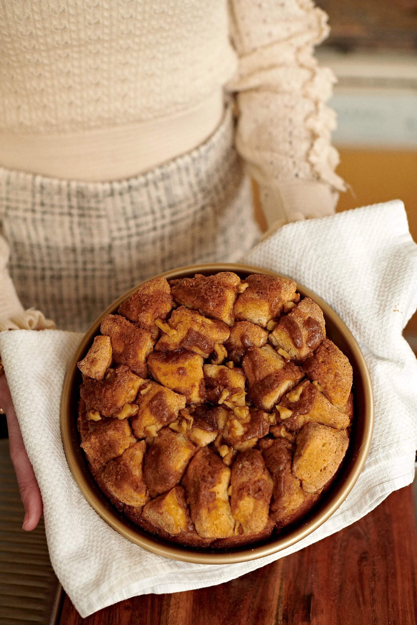 A bowl of rice crispy treat squares with nuts, held by a person in a white cloth napkin, on a wooden surface.