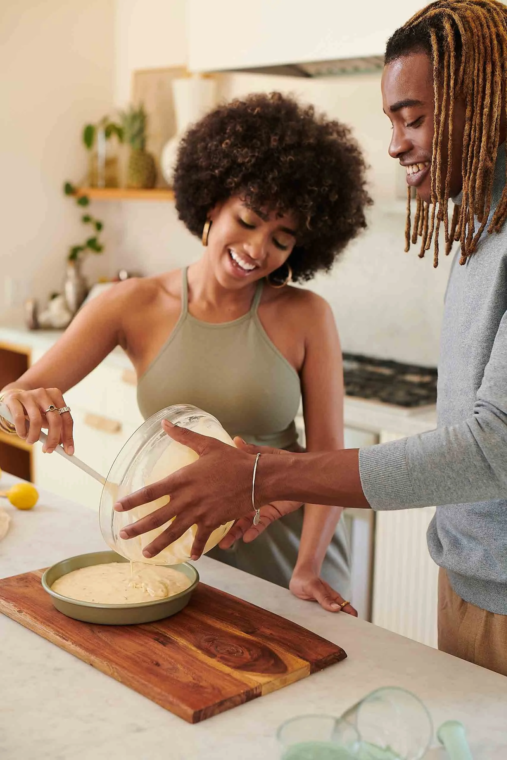 Two women preparing cake batter together in a modern kitchen, one pouring batter into a baking dish, both smiling and enjoying the activity.
