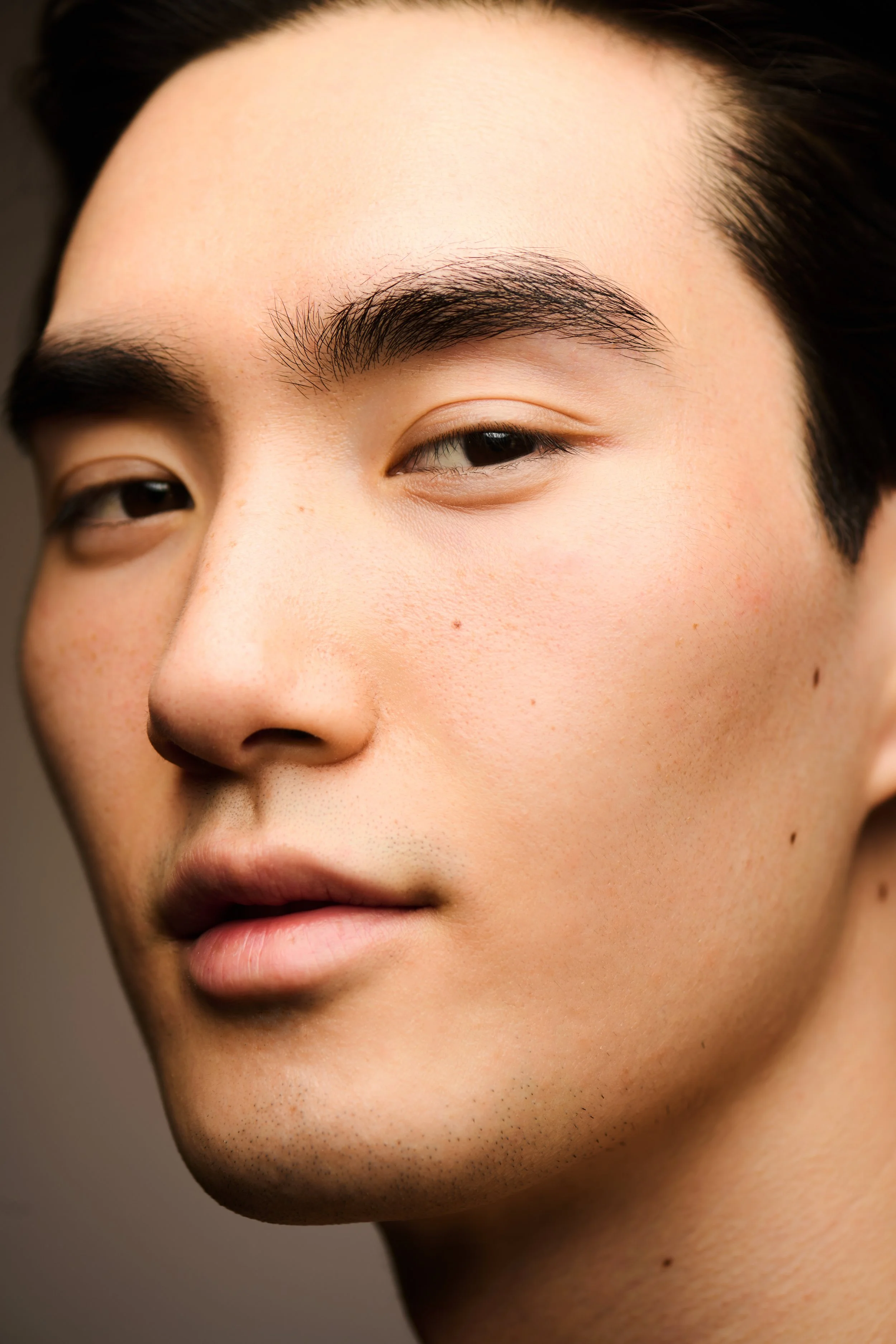 Beauty close-up of a man's face in soft daylight, skin texture and moles left visible.