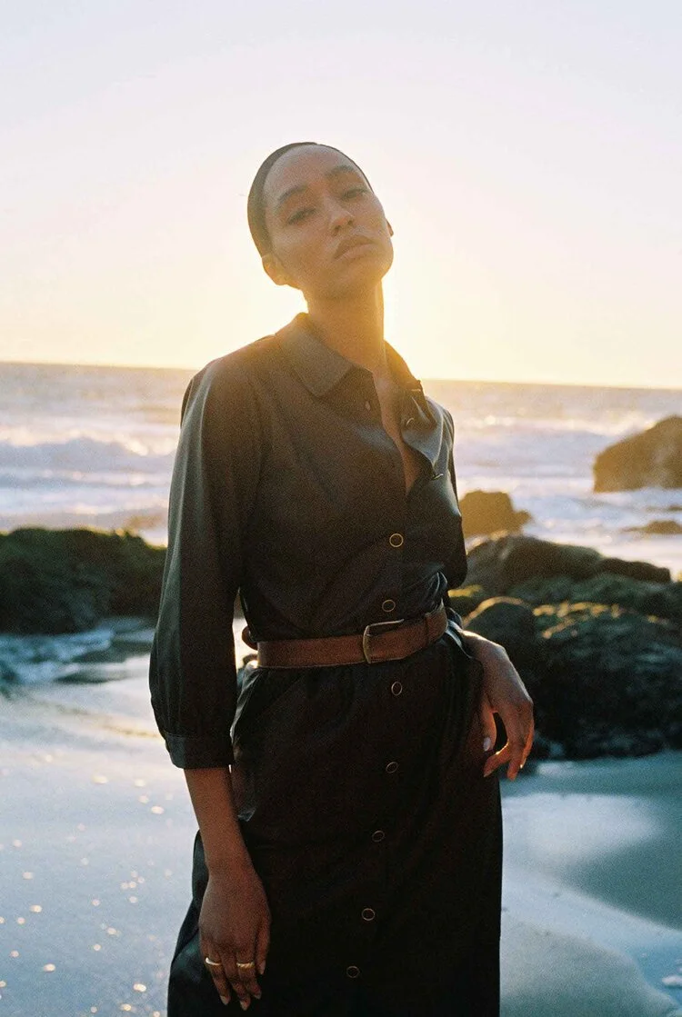 Test shoot portrait of a woman in an olive belted shirt dress on a rocky beach at golden hour.