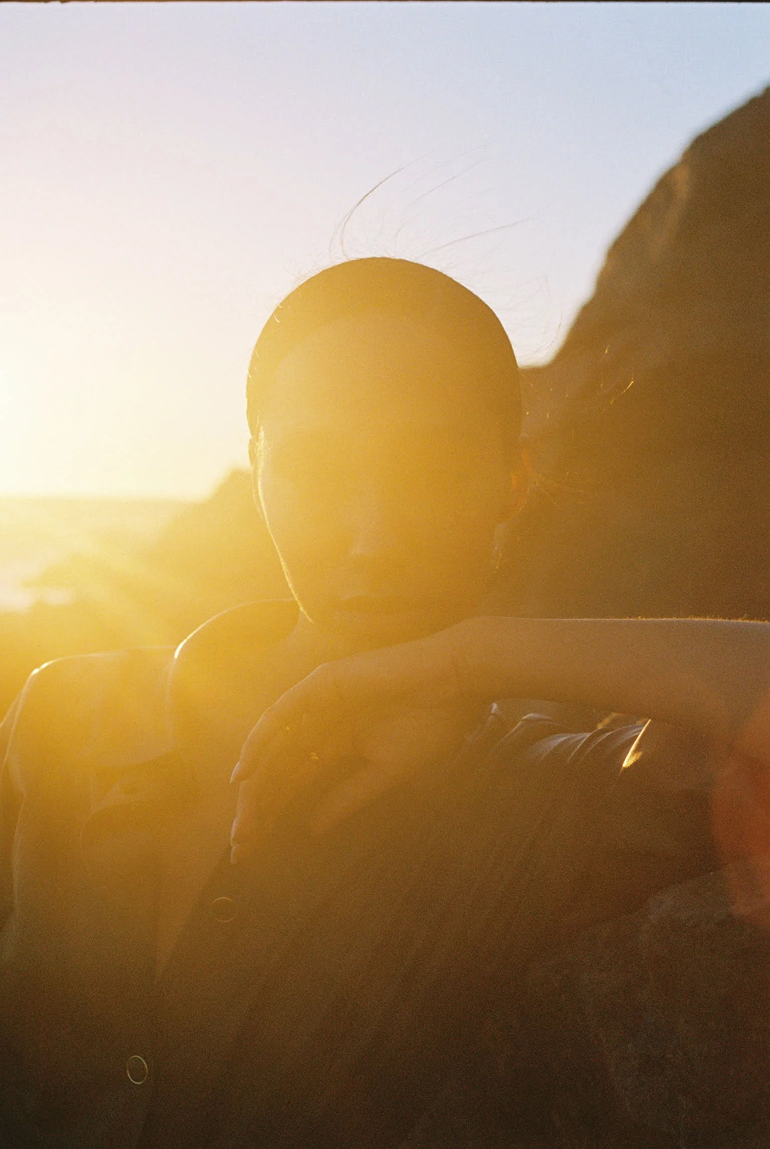 Silhouetted sunset test frame of a seated figure on the coast, sun burning through behind the shoulder.