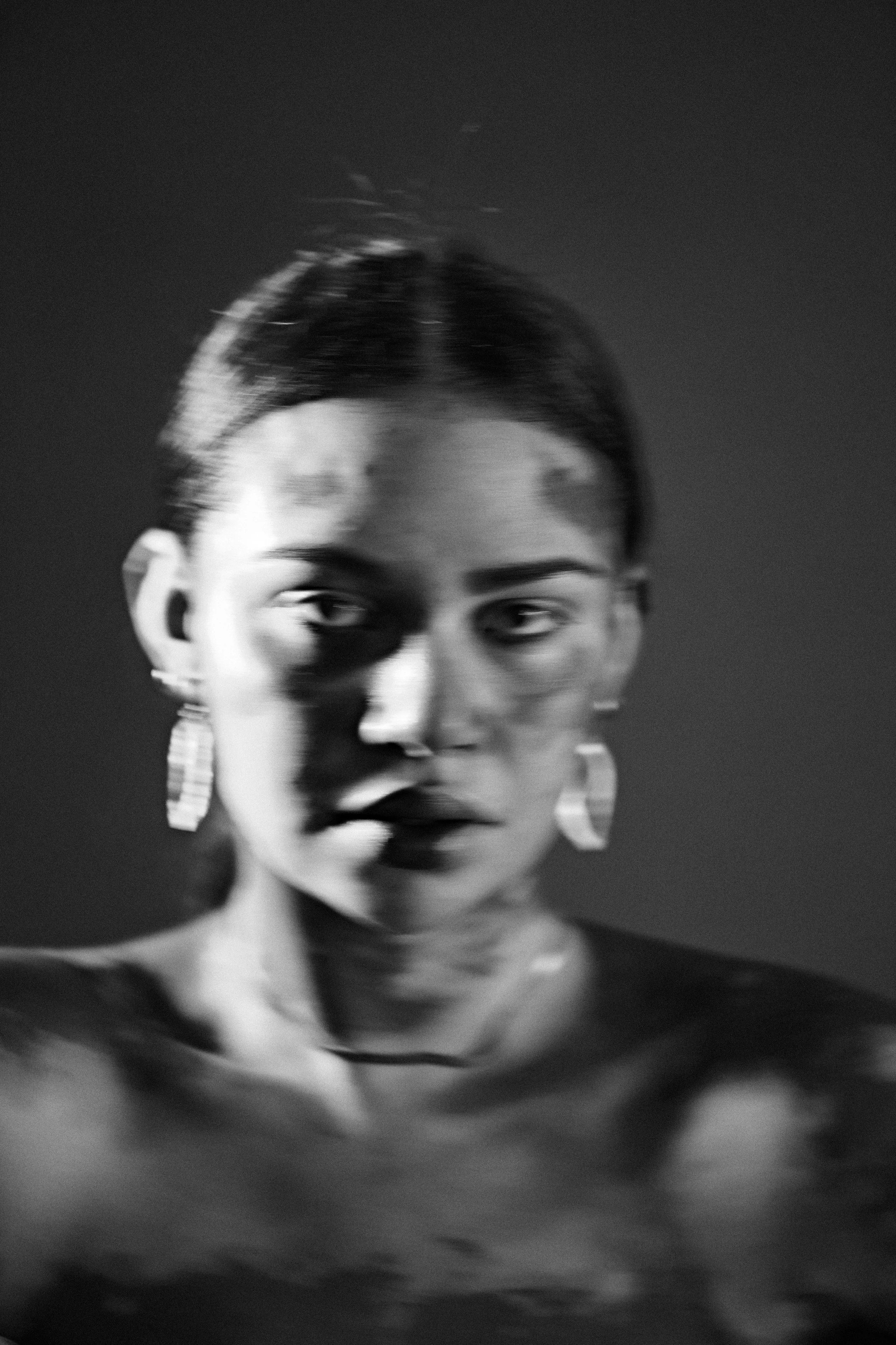 Black-and-white beauty test portrait of a woman in statement earrings, hard light casting patterned shadow across her face.