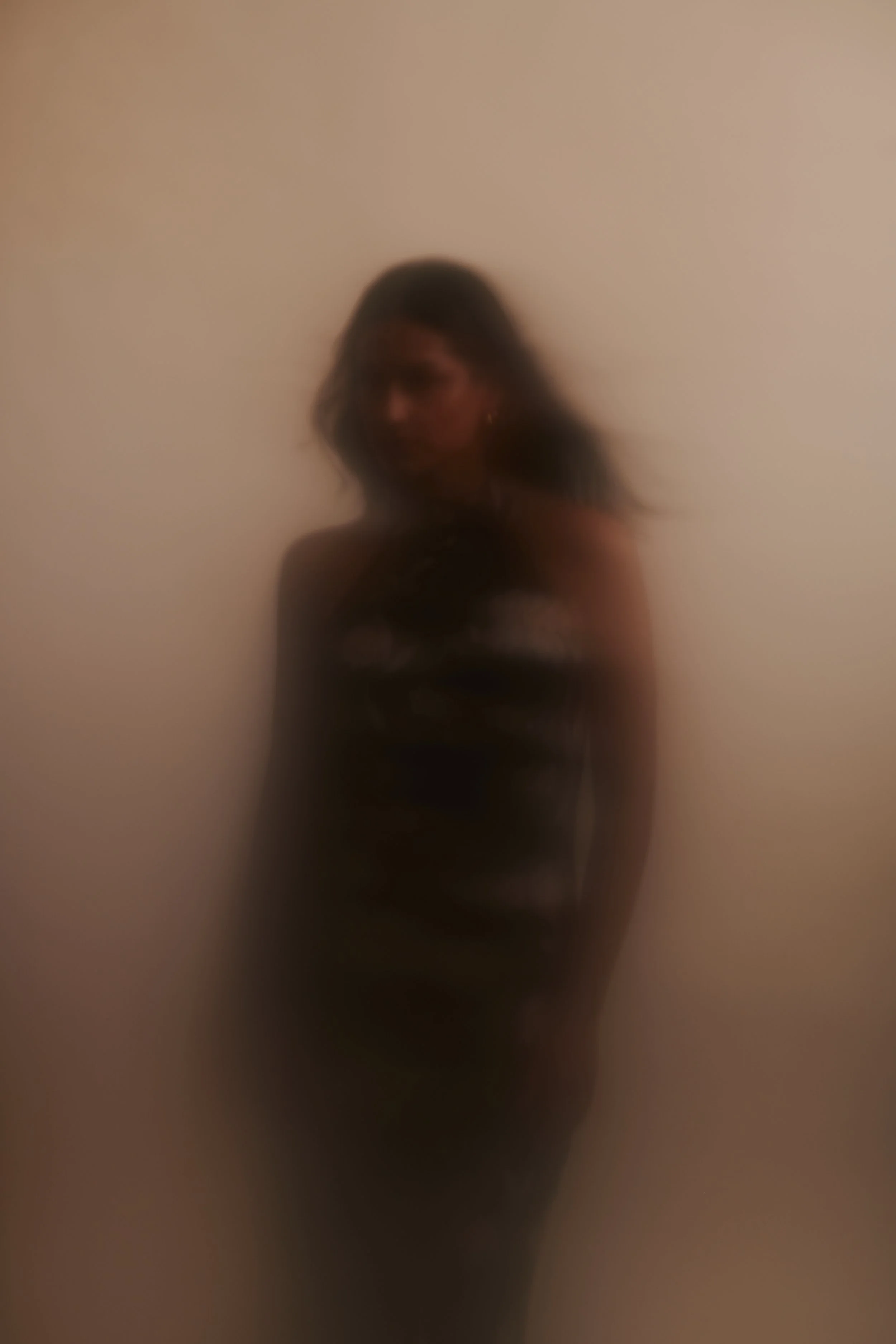 Motion-blurred test frame of a woman in a dark dress against a warm neutral wall.