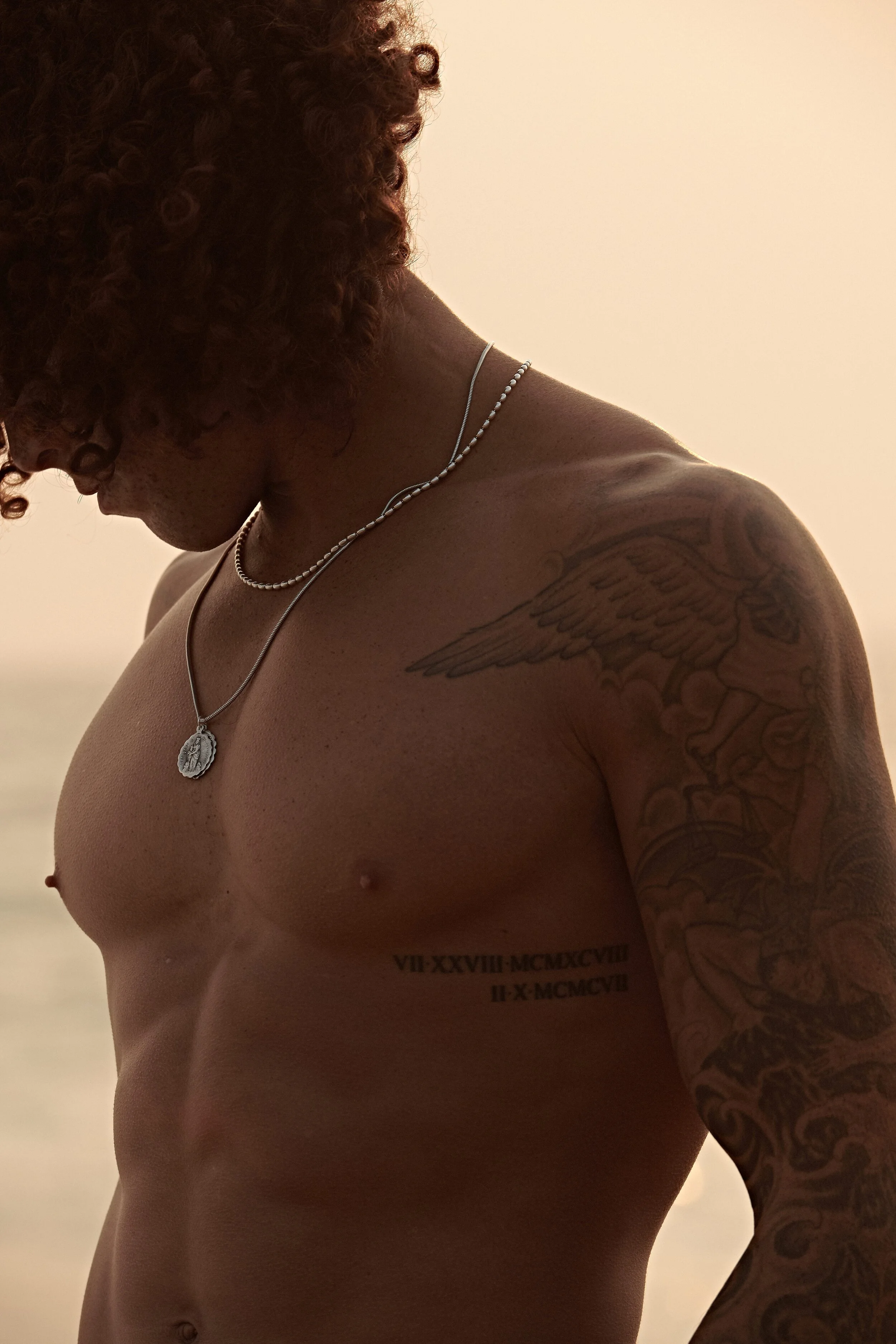 Warm outdoor test shoot of a shirtless man with tattoos and a pendant chain, shot in soft late daylight.