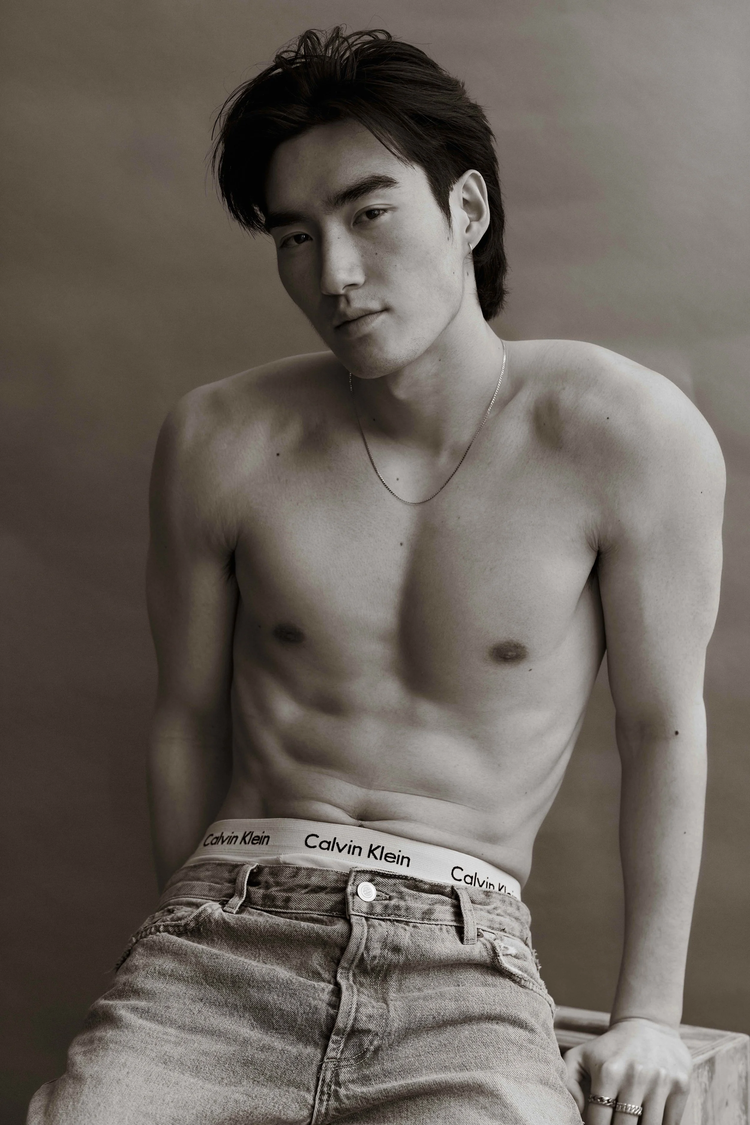 Black-and-white studio test portrait of a man seated in Calvin Klein jeans, photographed by Tony Moux in Los Angeles.