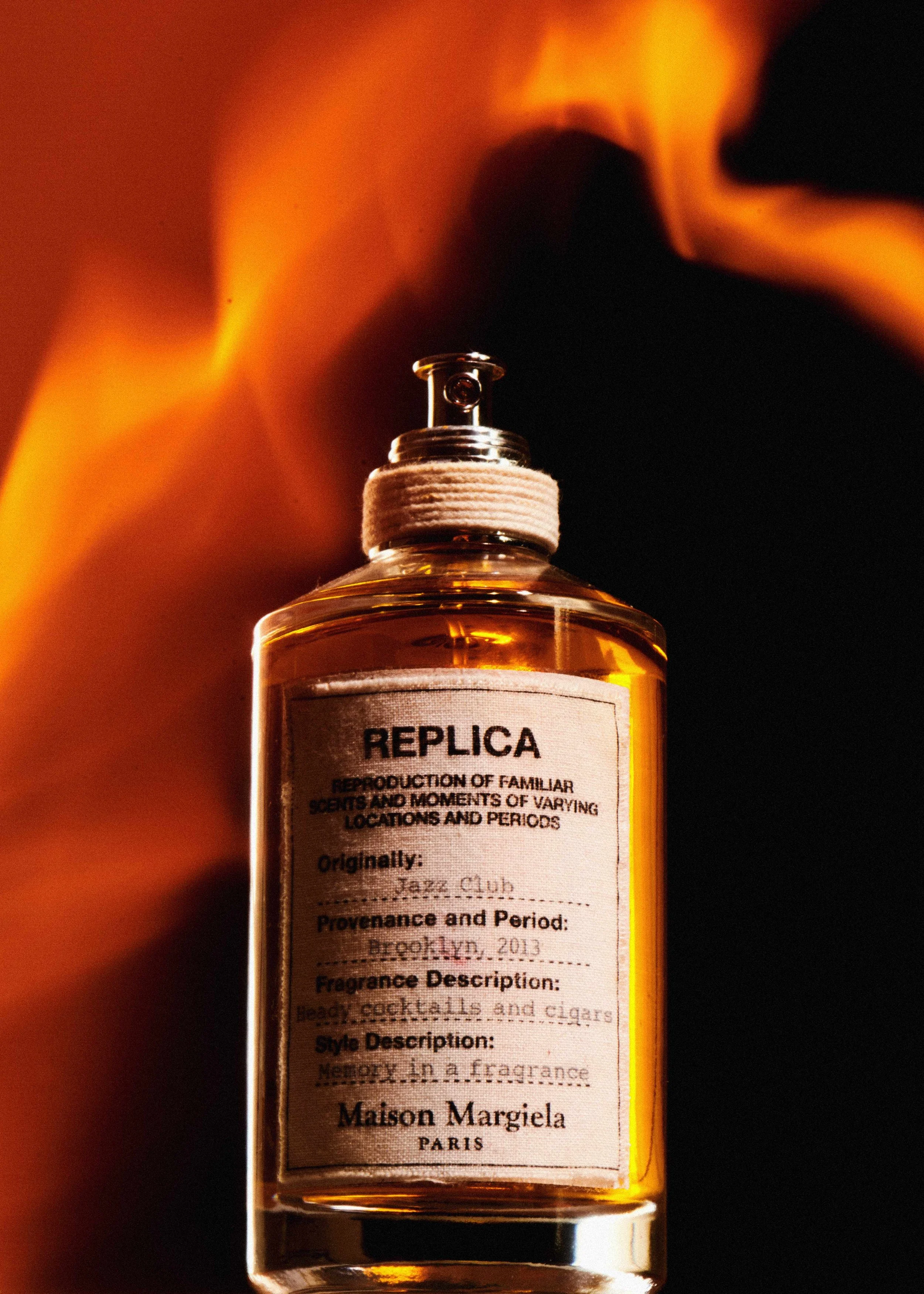 Fragrance still life of a Maison Margiela Replica bottle shot in front of open flame.