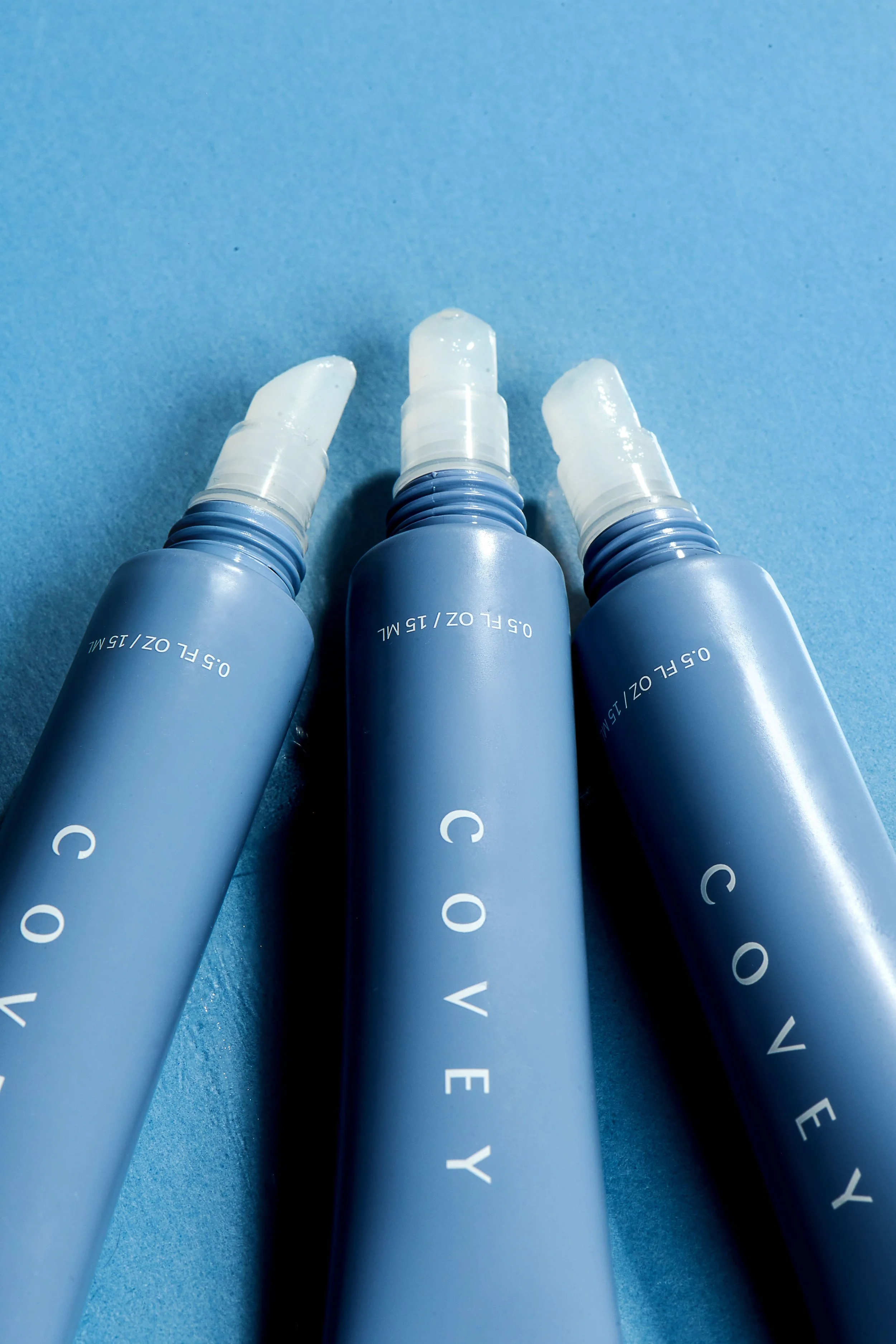Flat-lay product still life of three Covey tubes fanned on a mid-blue paper ground.