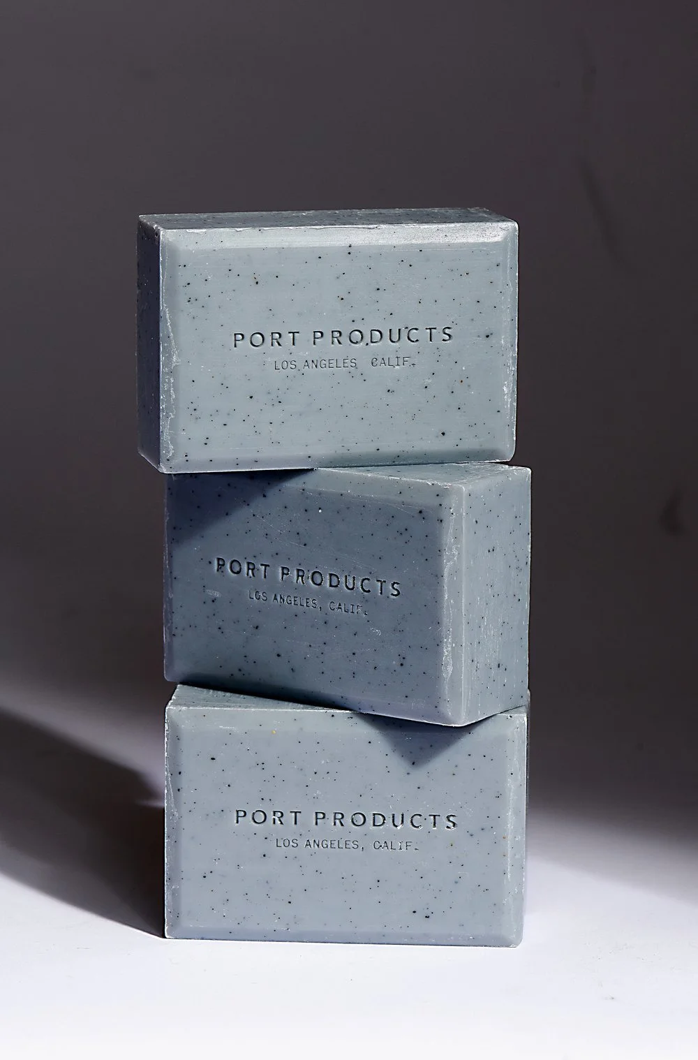 Still life of three stacked Port Products soap bars, hard light and clean shadow on a neutral set.
