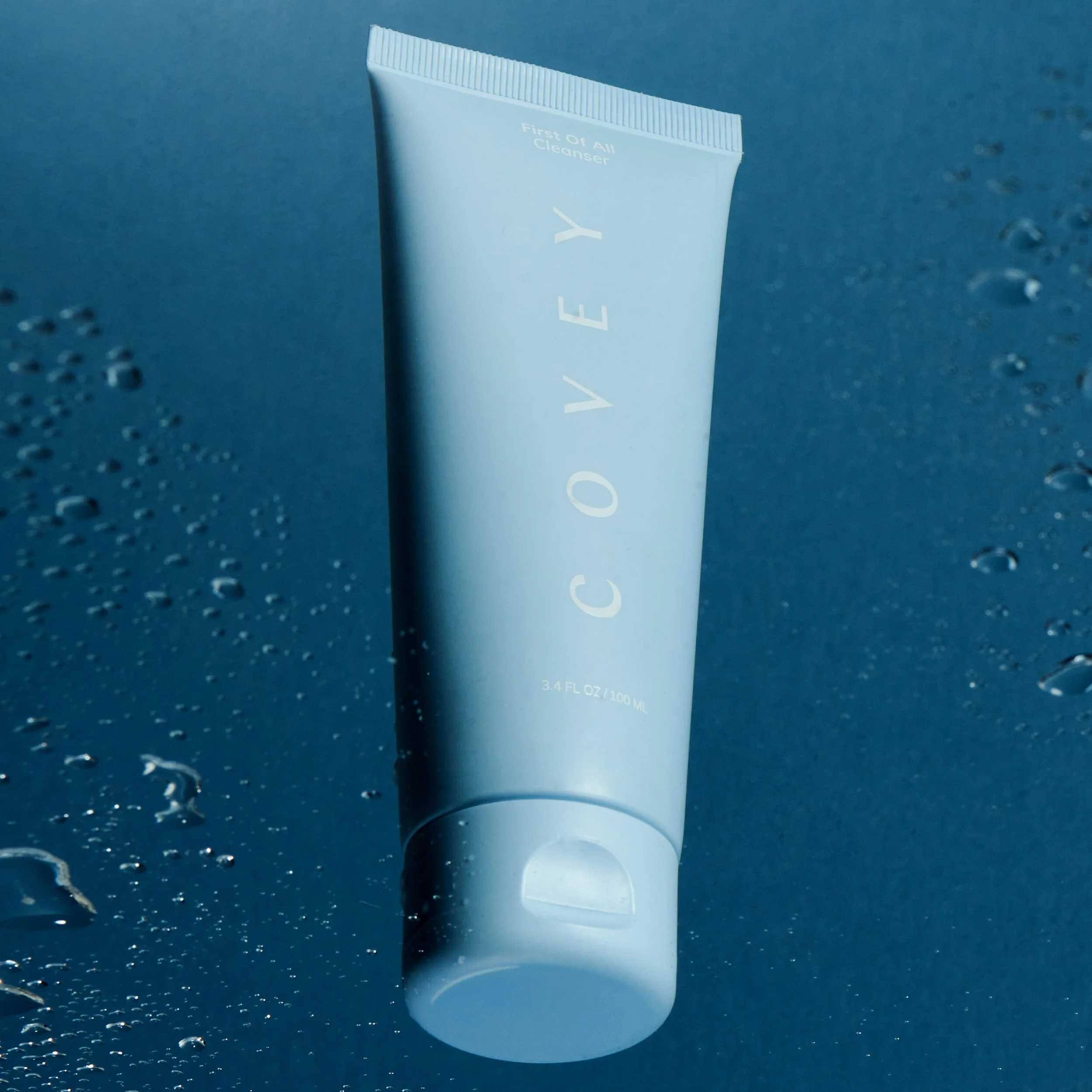 Product still life of a Covey cleanser tube on a wet blue surface scattered with water droplets.