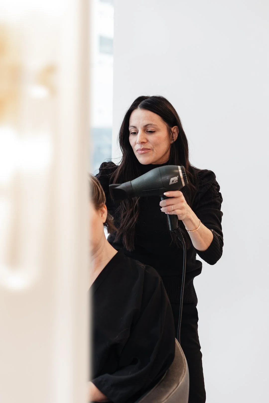 A hairstylist blow-drying a woman's hair in a salon.