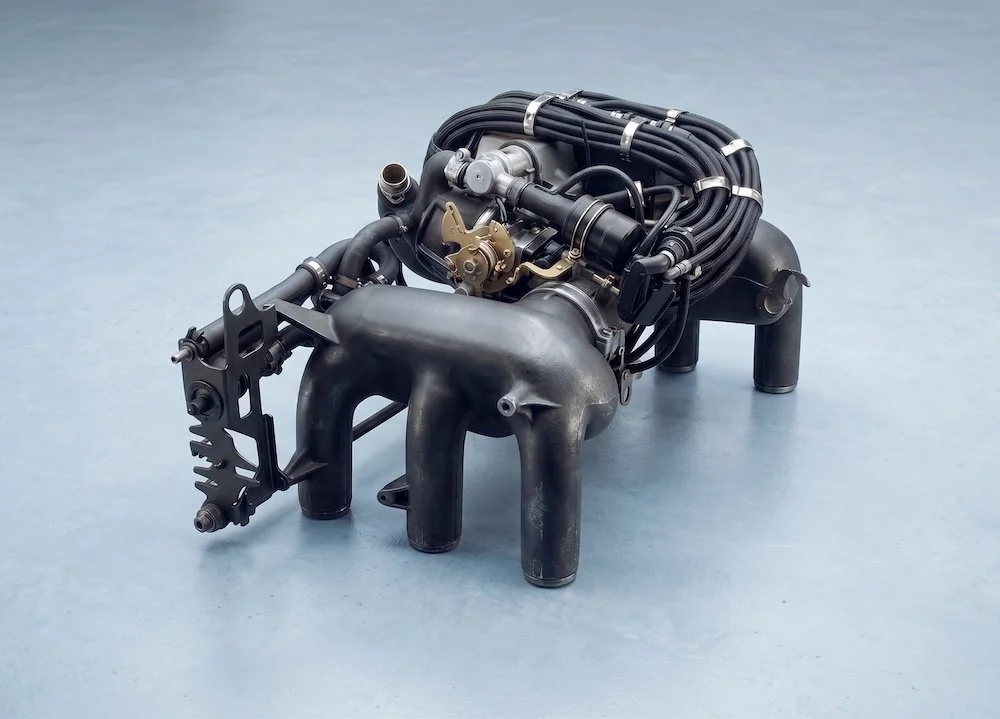 A hypercar engine with black cables, metal parts, and gray pipes, placed on a light blue surface.
