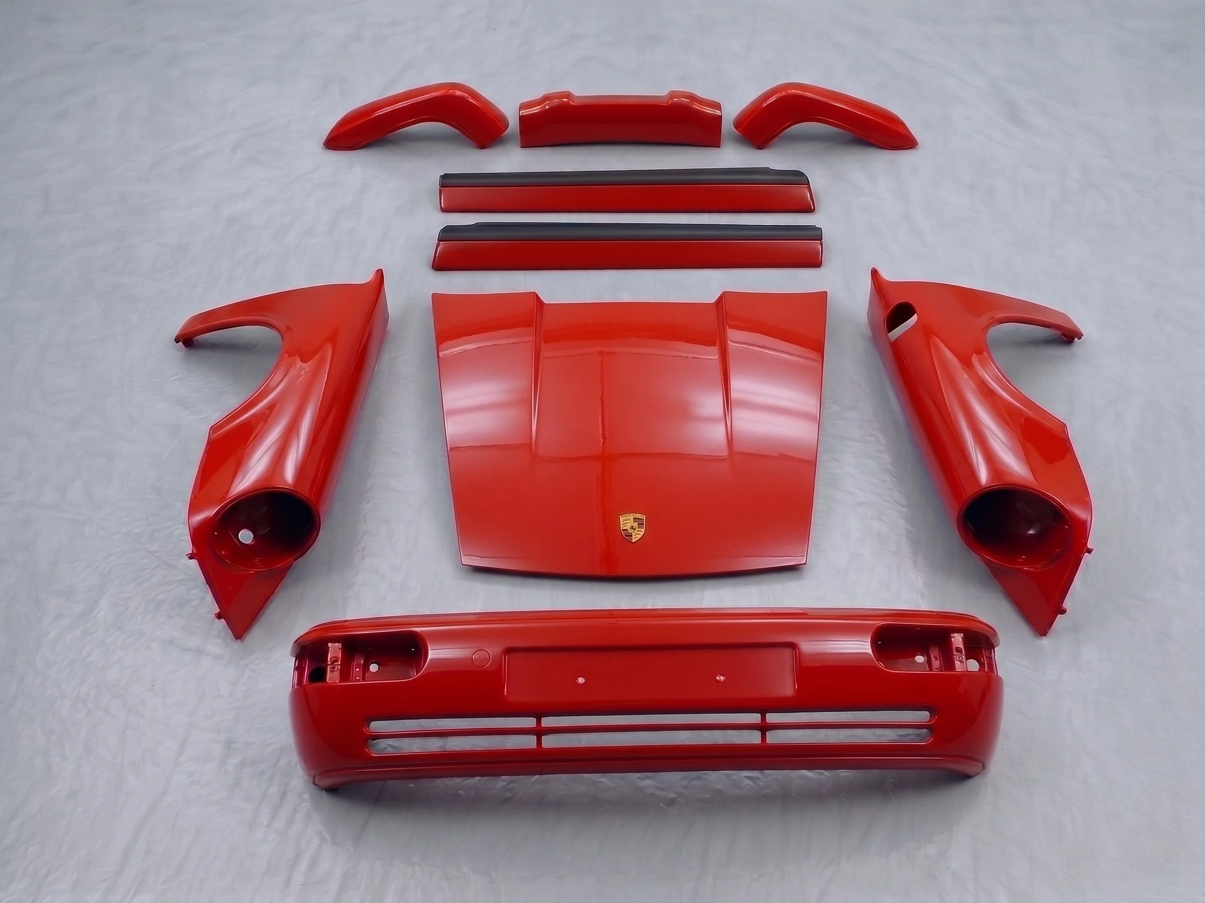 Disassembled red car parts including two side mirrors, a rear wing, and other components laid out on a white surface.