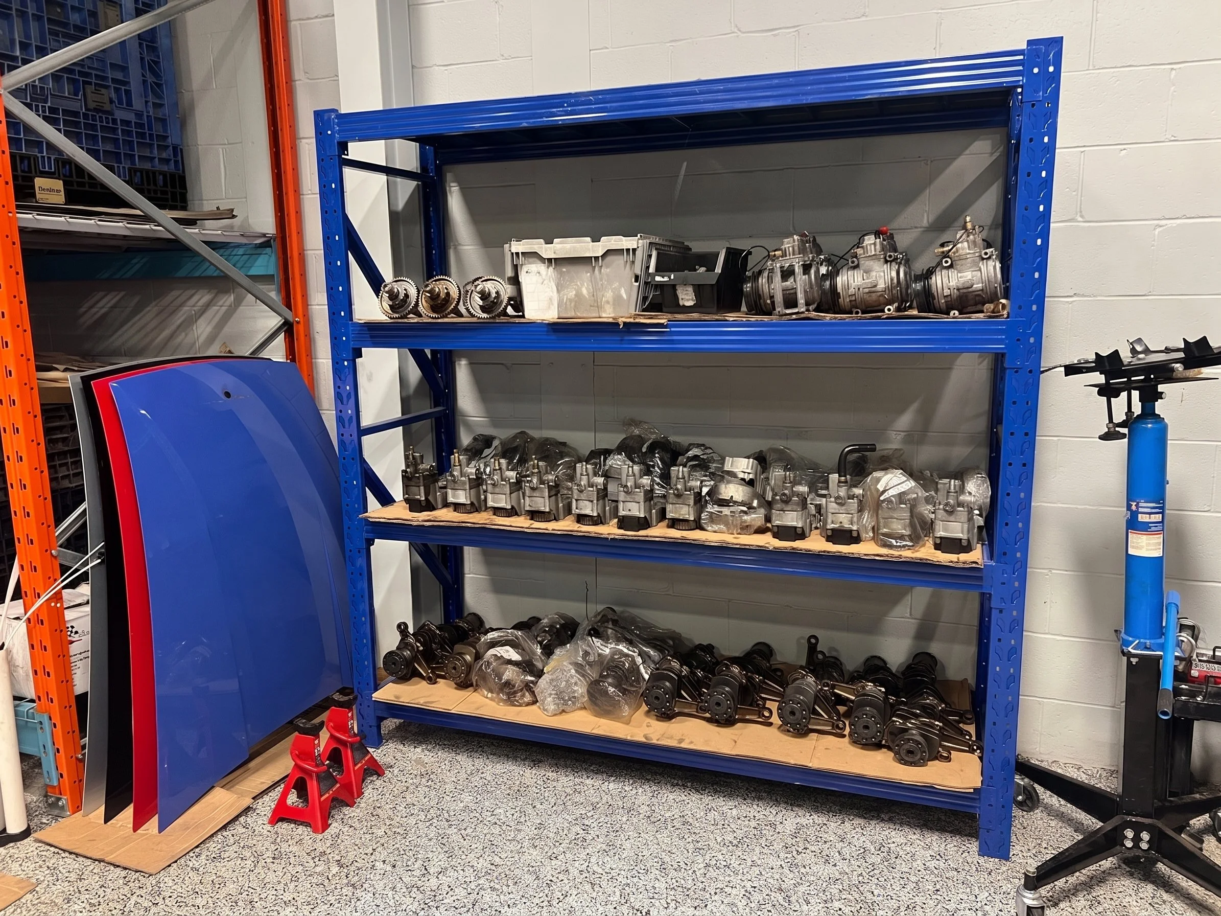 Blue industrial shelving unit holding multiple automotive engine parts and components in a workshop or storage area.