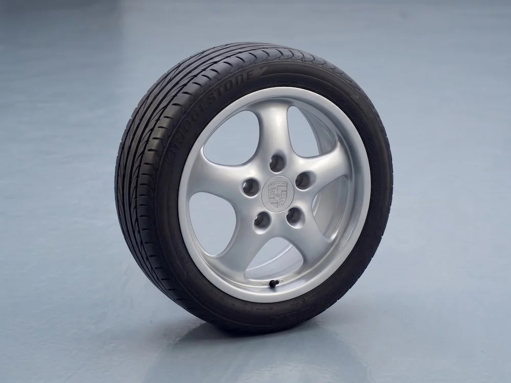 A car tire with a silver alloy rim and a black Bridgestone tire, placed on a light surface.