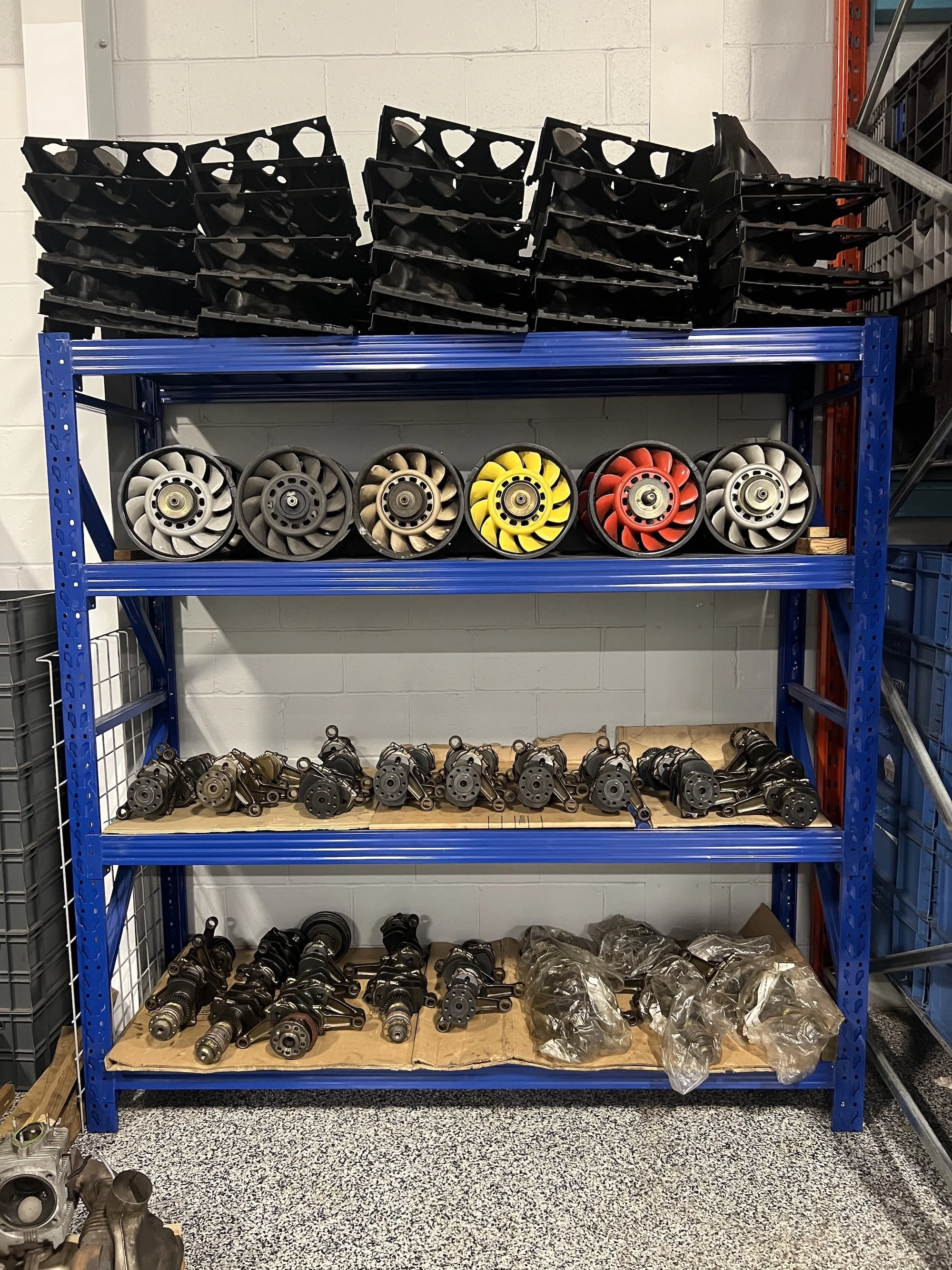 Shelves filled with automotive engine components such as turbochargers and intake manifolds in a workspace.