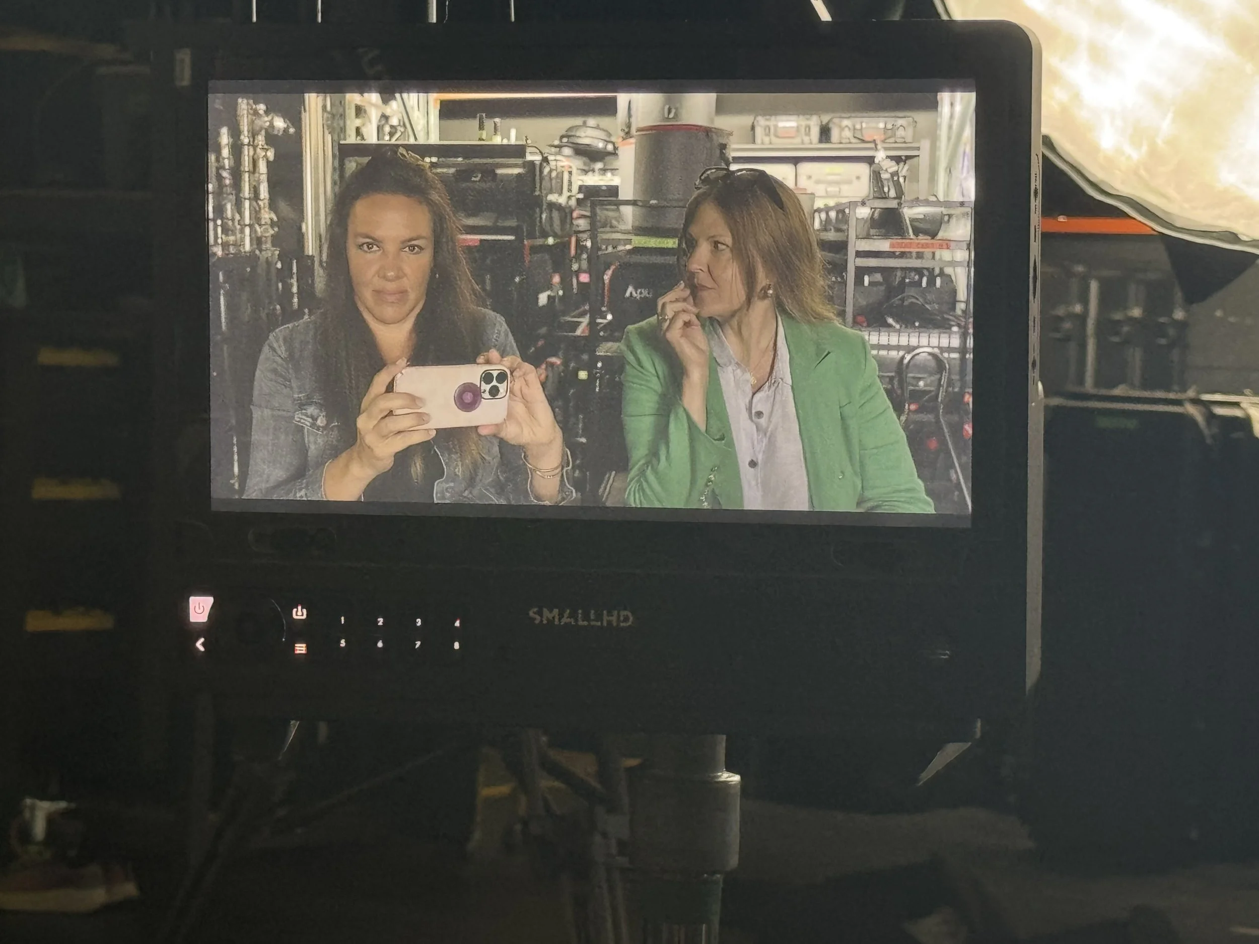 Two women taking a selfie in a storage room with industrial equipment and shelves in the background.