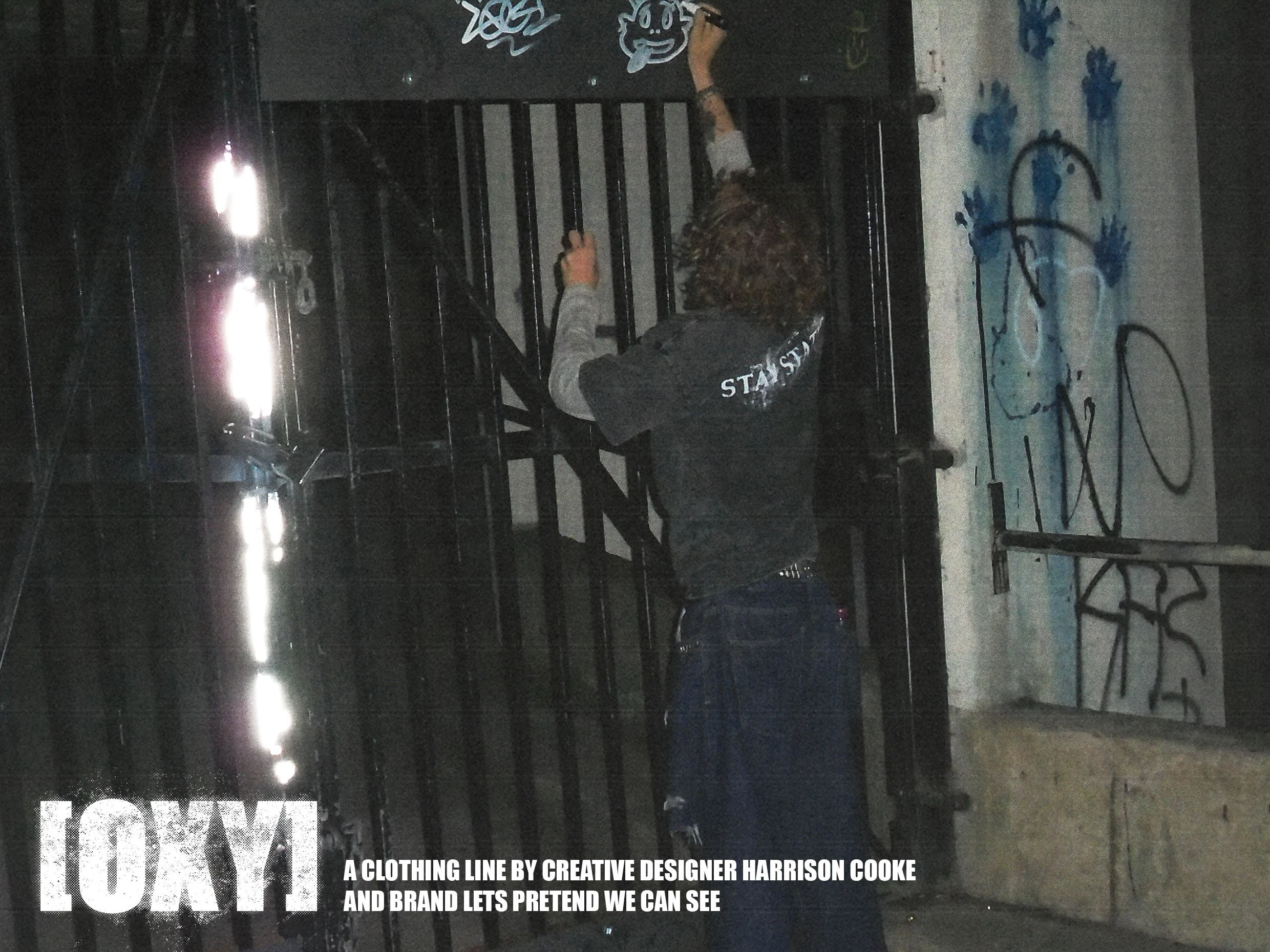 Dark-colored hanging clothing display with graffiti art on the wall behind. Text at the bottom reads 'A clothing line by creative designer Harrison Cooke and brand lets pretend we can see'.
