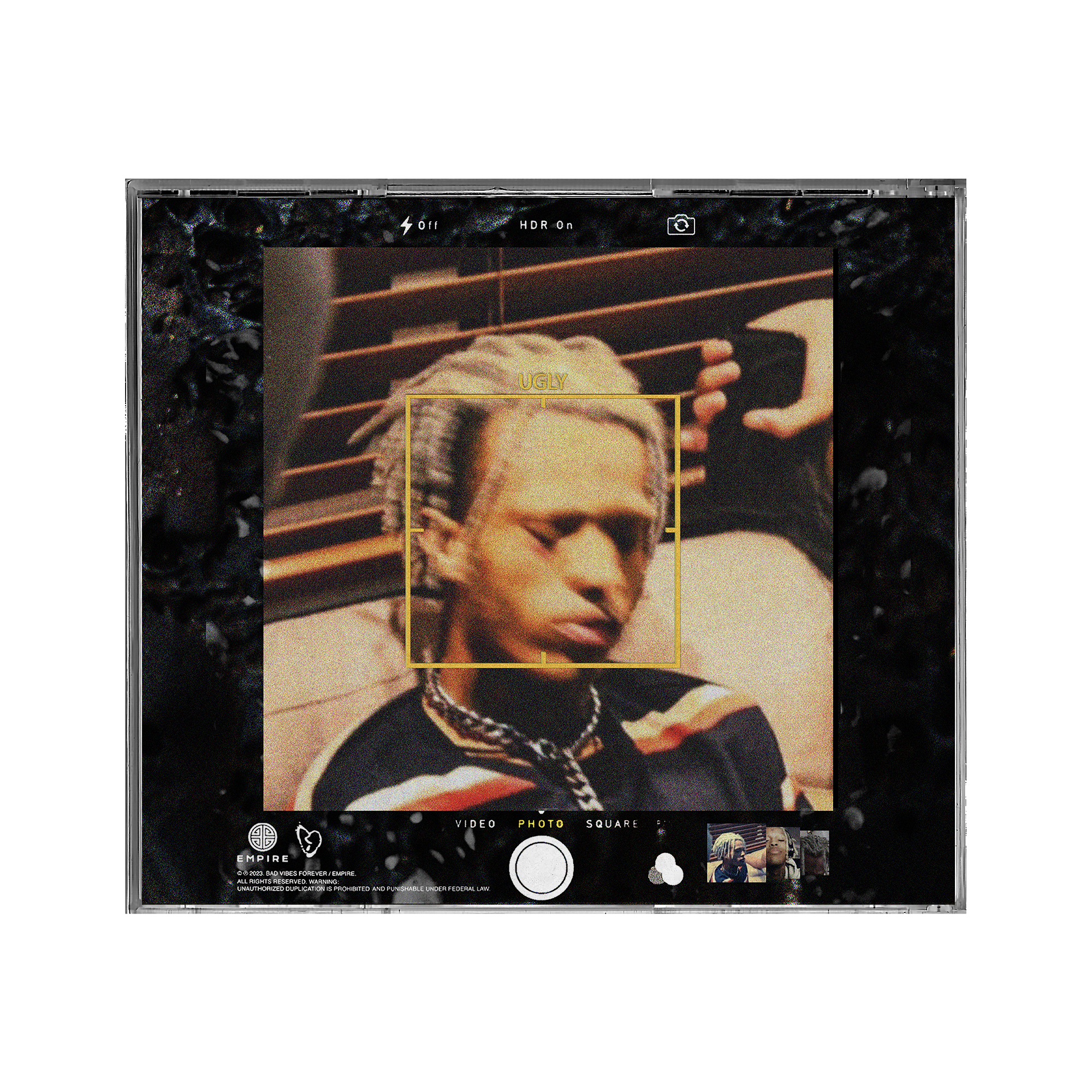 A smartphone screen capturing a selfie of a person with blonde hair and a black top, with the photo app interface visible and the word 'UGLY' in yellow text over the person's face.