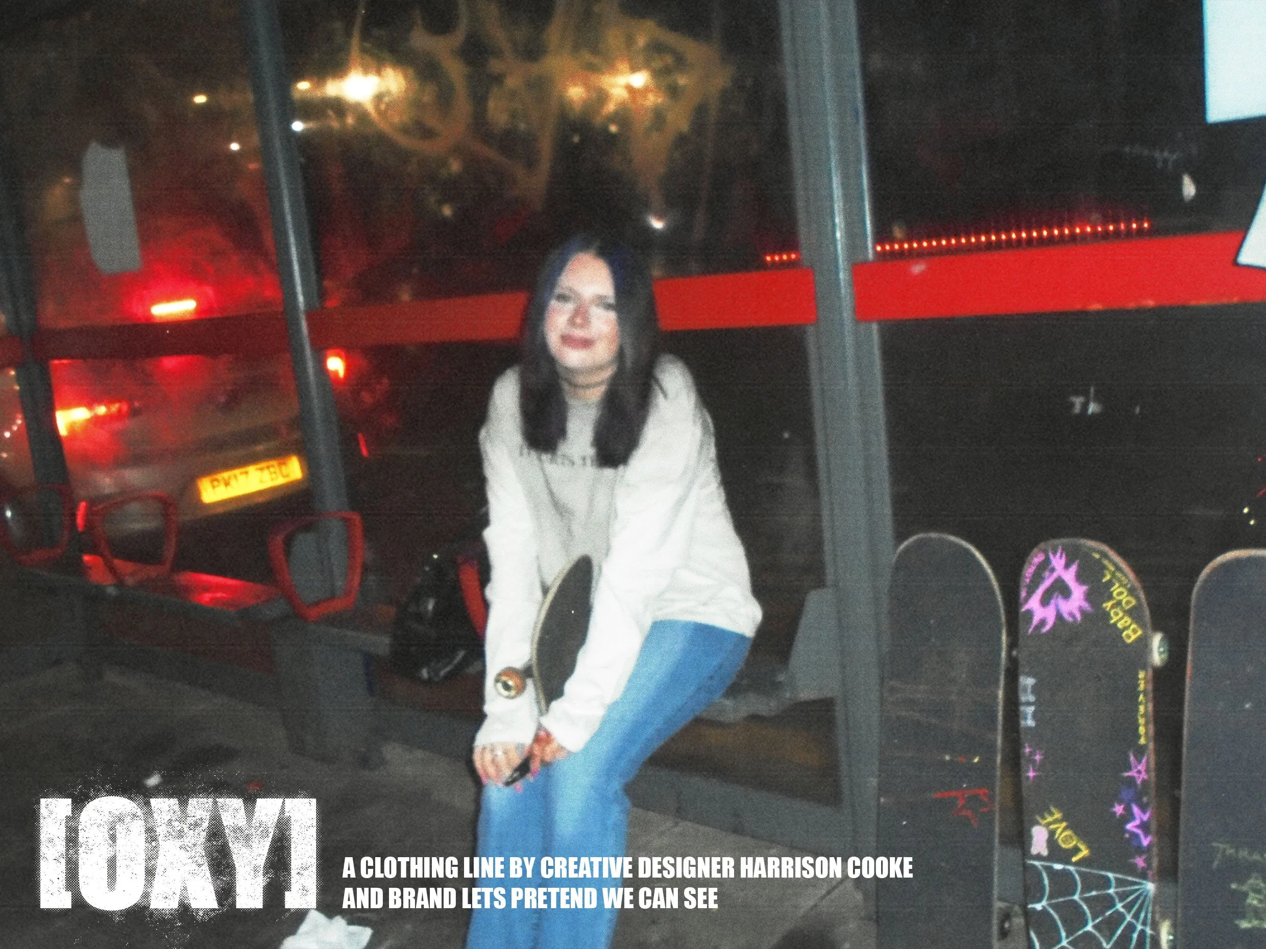 A woman with long dark hair and a white sweatshirt sitting at a bus stop at night, with reflections of city lights and a bus in the background.
