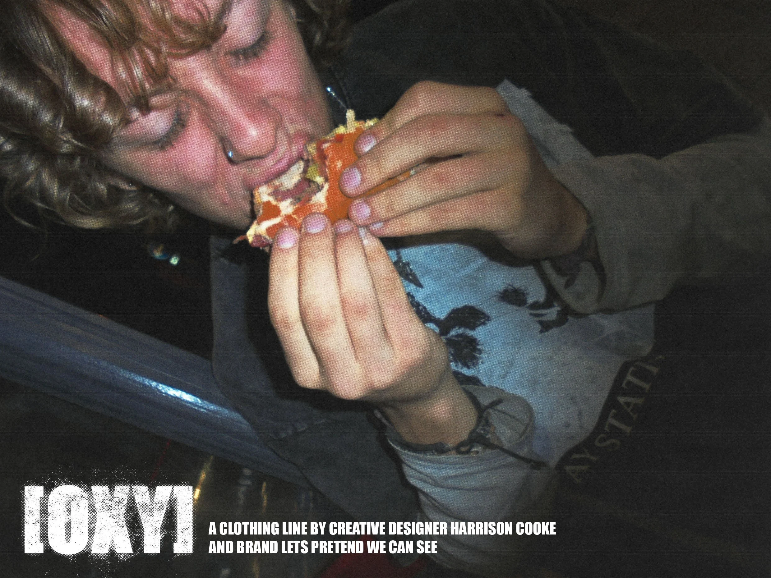 A person with curly hair and a nose piercing is eating a slice of pizza inside a vehicle.