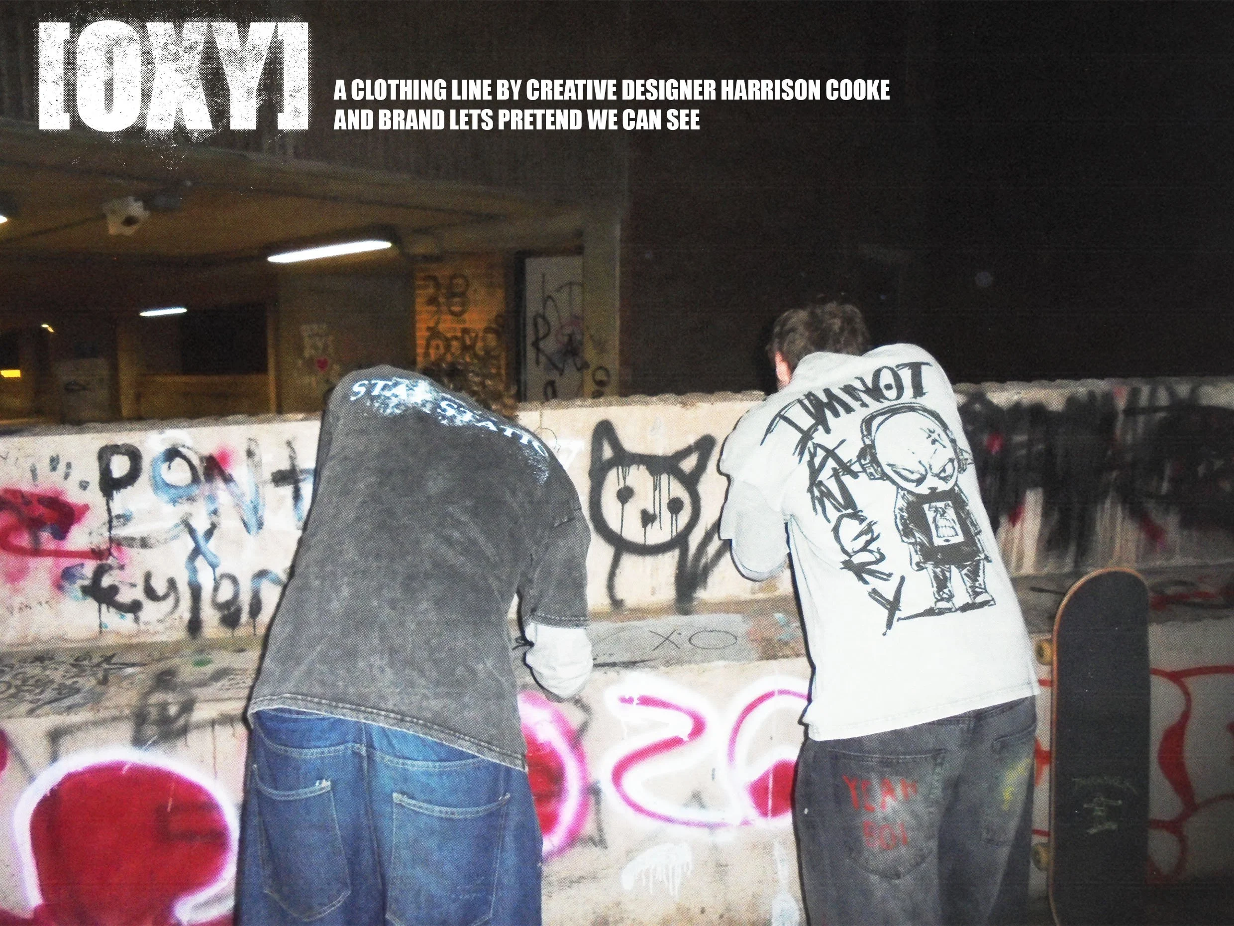 Two people with their backs turned, wearing hoodies, sitting in front of a graffiti-covered wall at night. The wall has various graffiti art and spray paint markings.