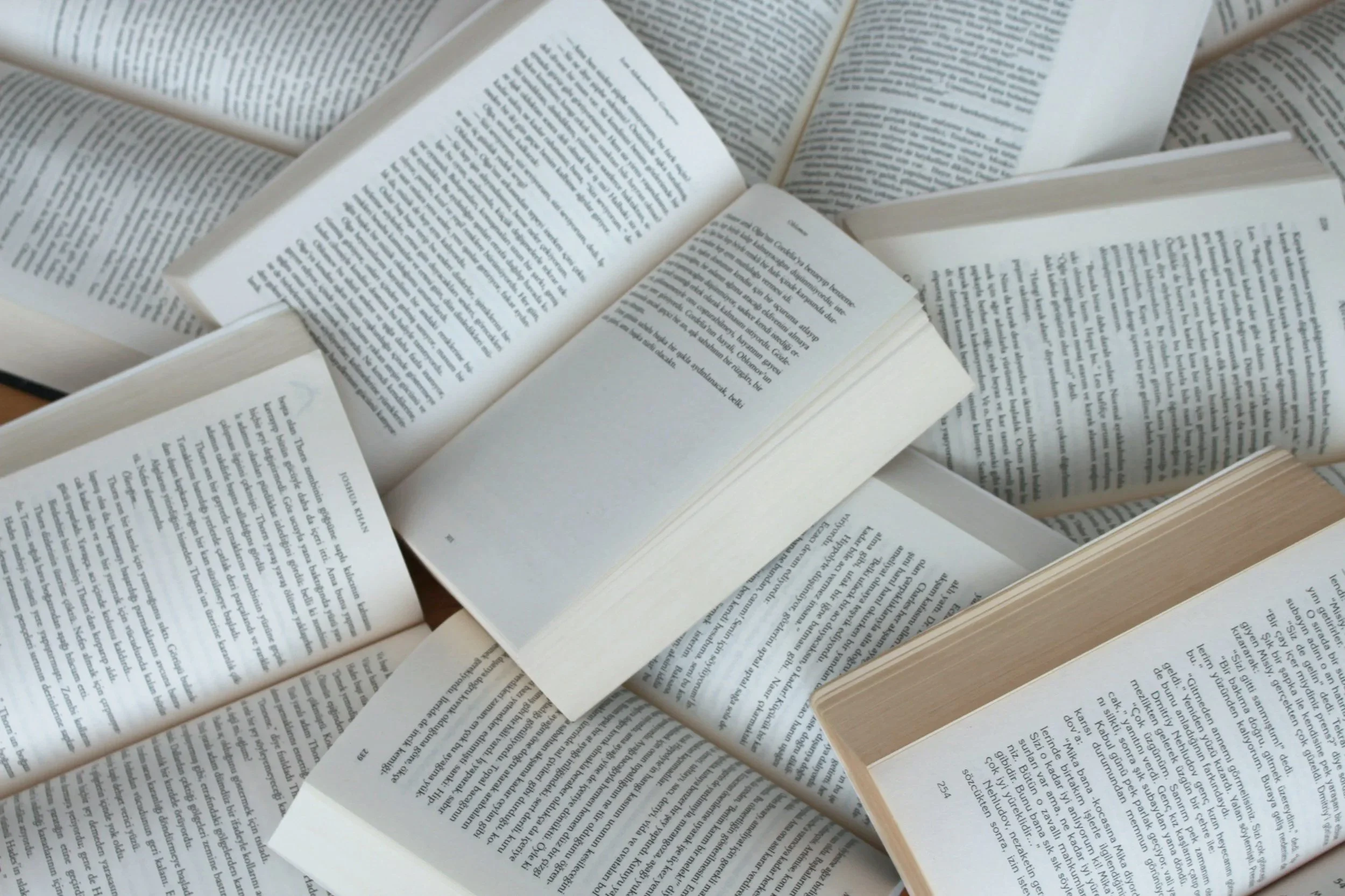 Multiple open books with pages displaying text, stacked and arranged in a disorganized manner.