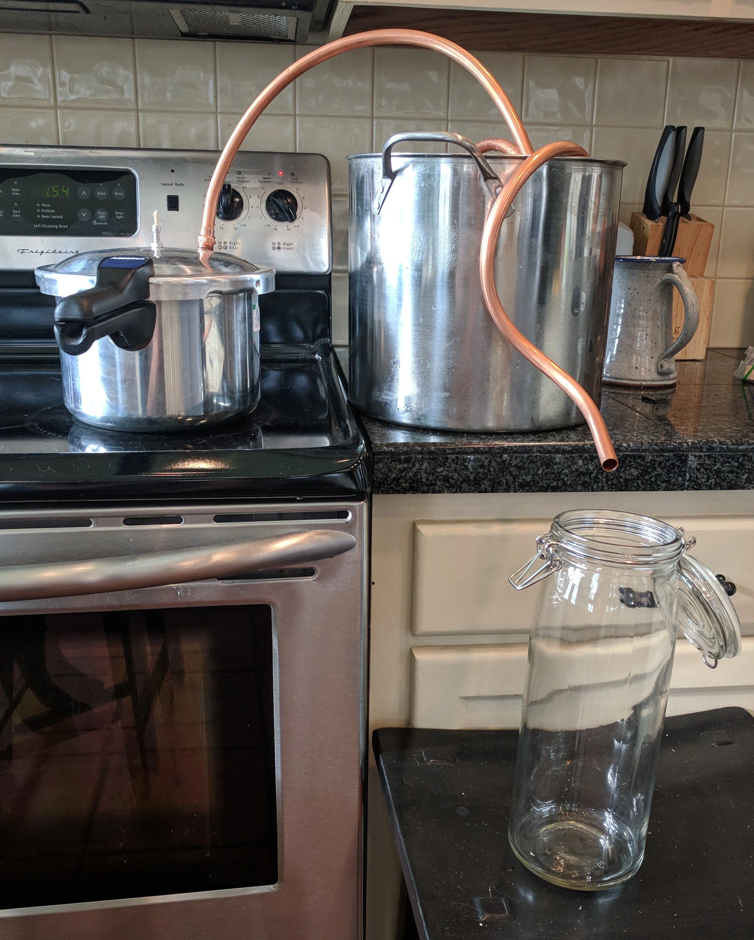 A kitchen with a stovetop, a coffee pot, a large metal container, a glass jar, and a knife block on the counter.