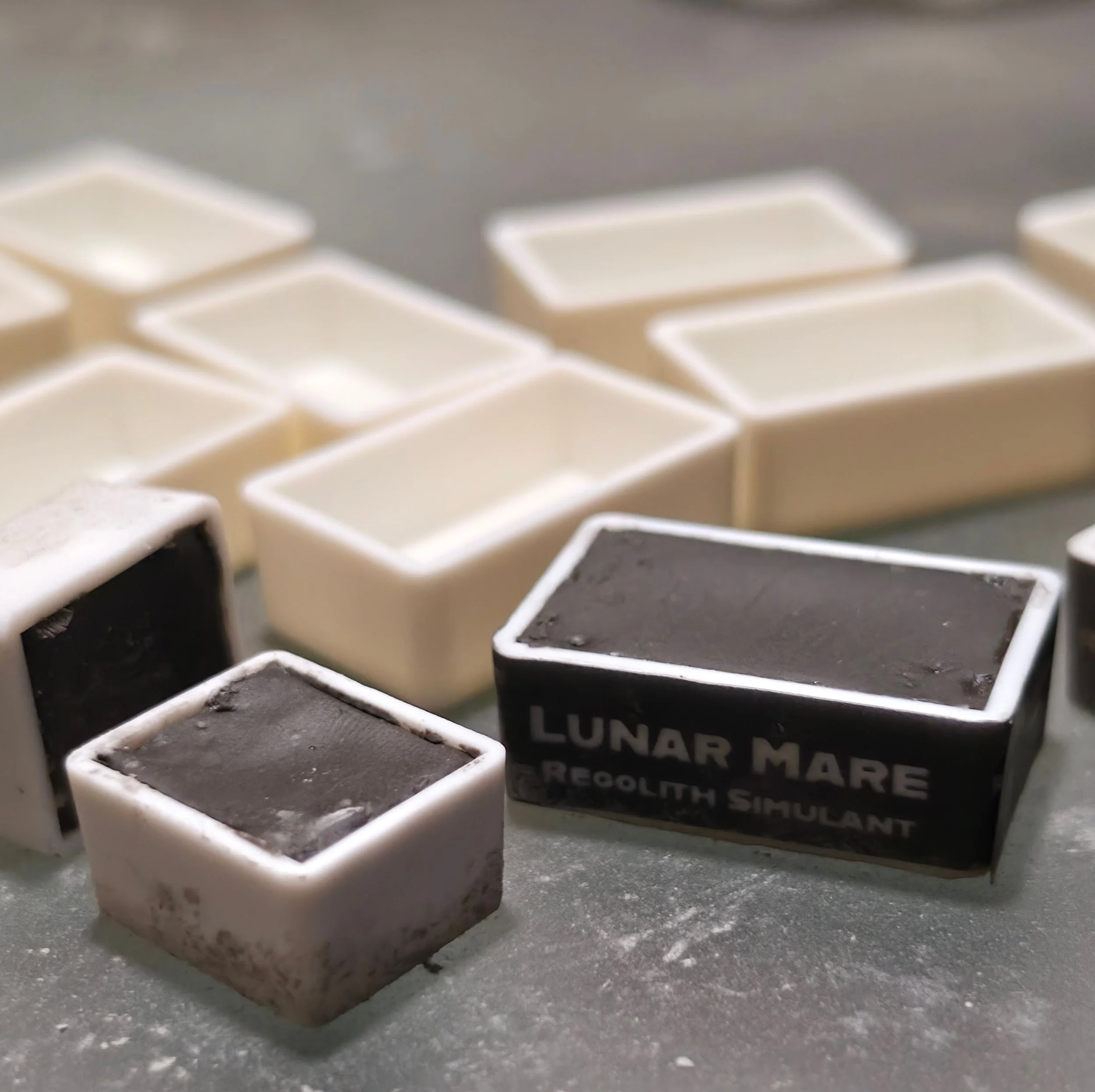 Close-up of a single dirty ice cube on a gray surface, with several more ice cubes blurred in the background. A sign in the background reads 'Lunar Market'.