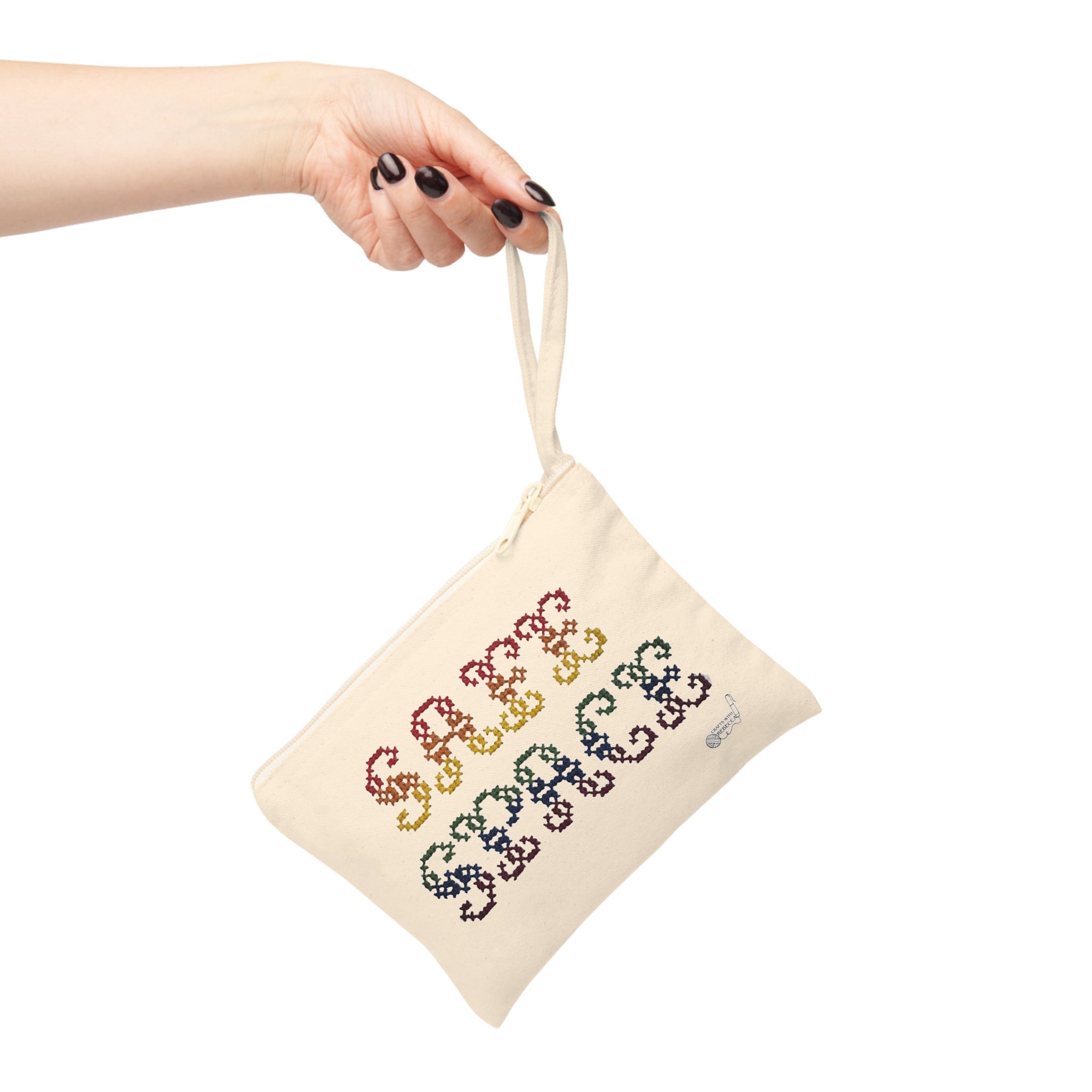 A hand with black nail polish holding a beige fabric with colorful cross-stitch embroidery.