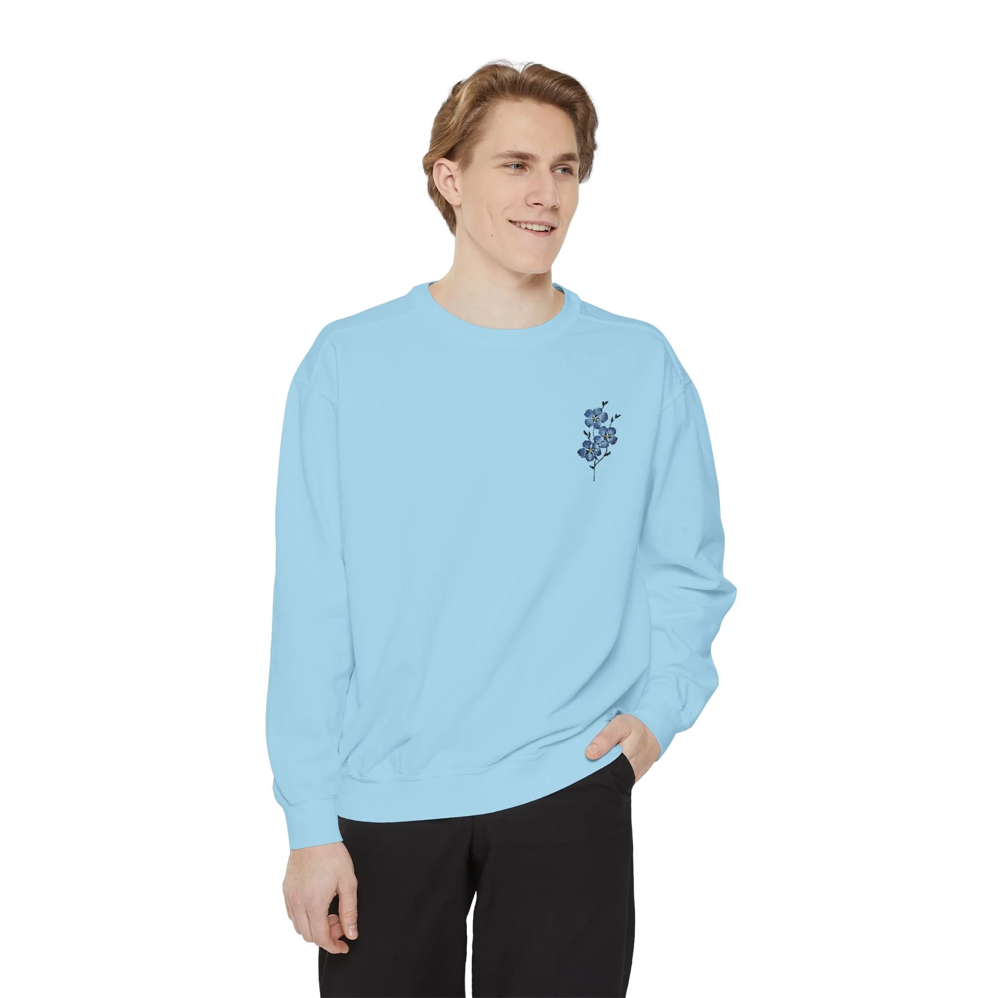 Young man wearing a light blue sweatshirt with a floral design, standing against a white background.