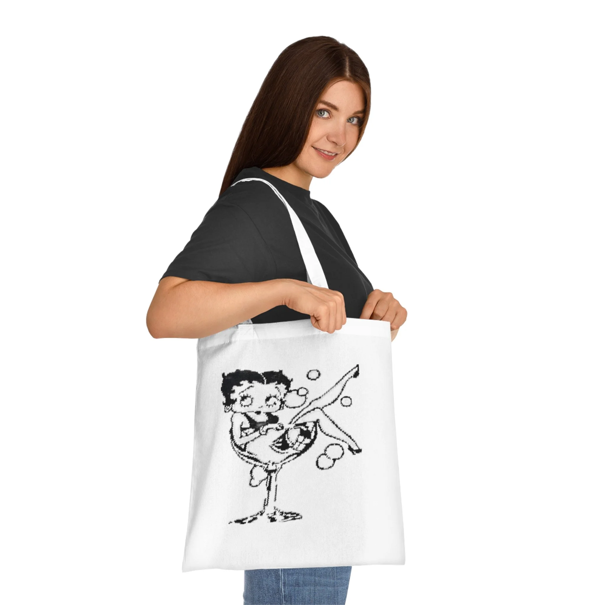 A person holding a white tote bag with a black graphic design of a cartoon character and bubbles, wearing a black shirt and blue jeans.