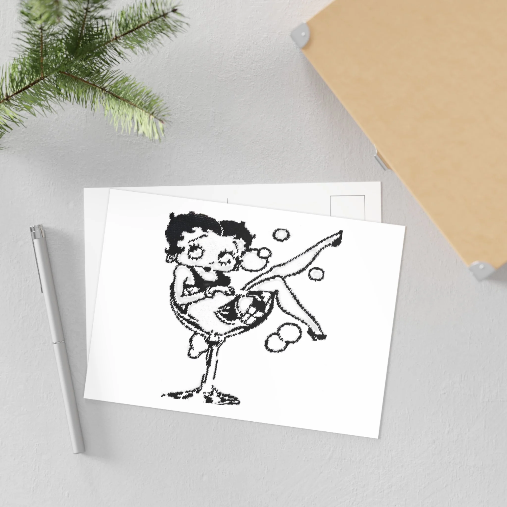 A printed sheet with a pixel art portrait of a cartoon character, placed on a white desk next to a silver pen. A sprig of green pine is hanging from the ceiling. Part of a wooden cabinet and a piece of paper with black text are in the background.