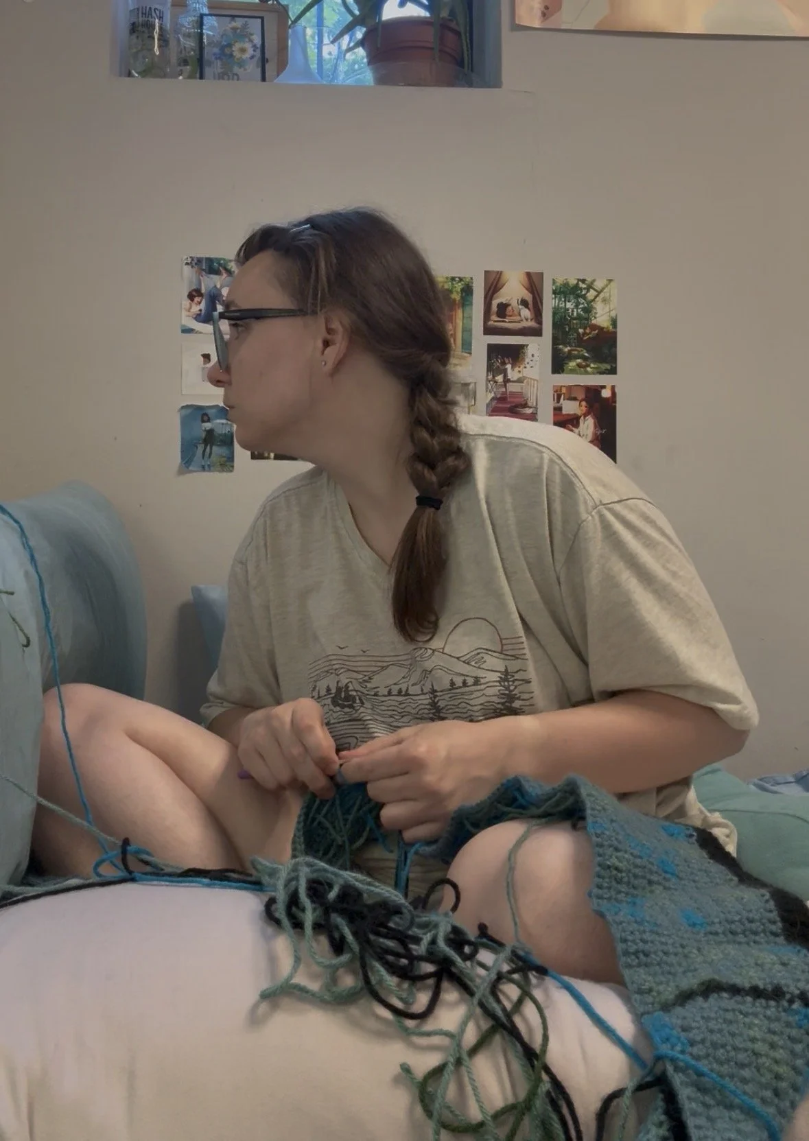 Rebecca is crocheting with multiple yarns and a crochet hook, in a room decorated with photos and artwork on the wall.