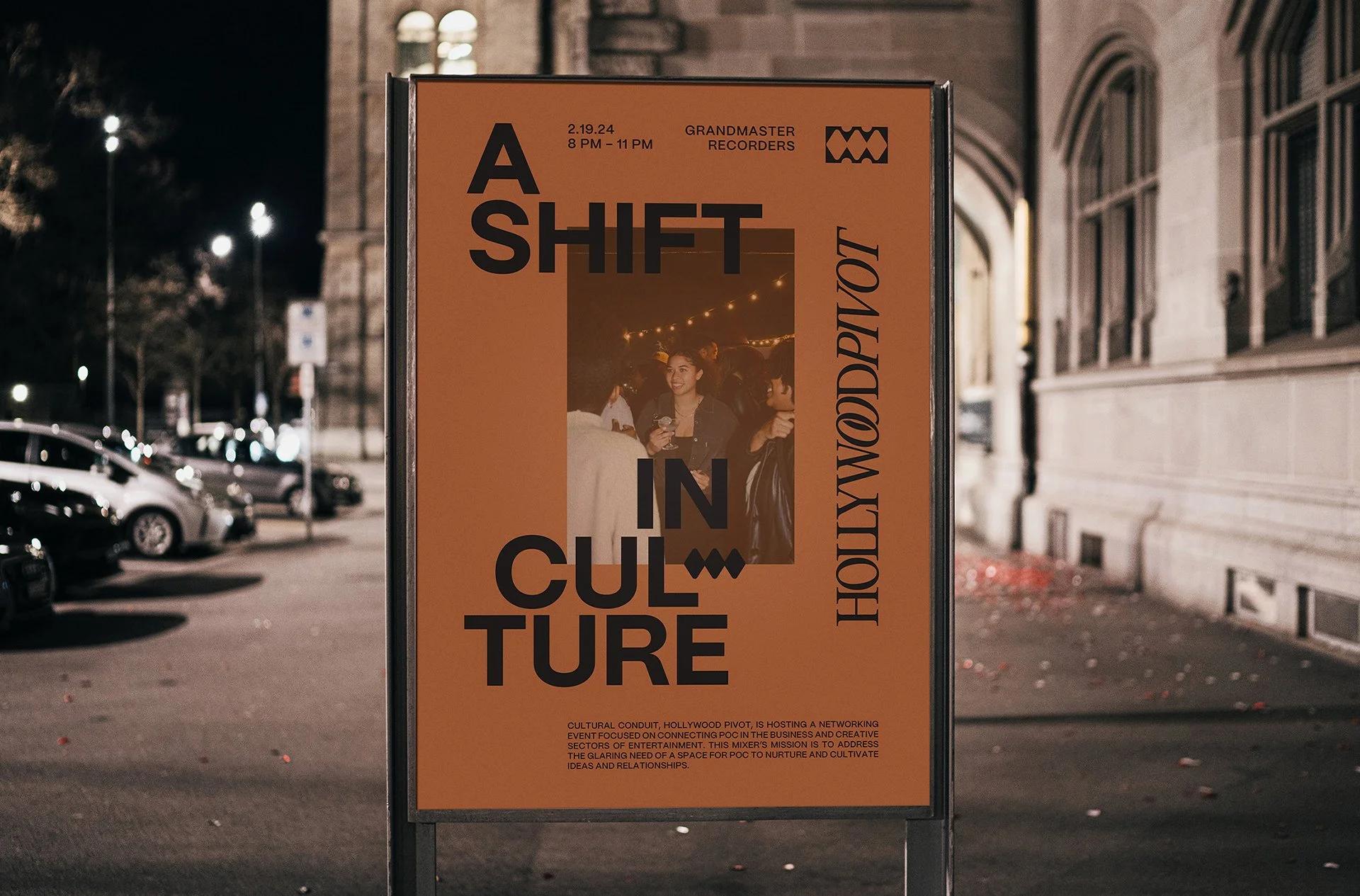 A vertical orange poster placed outdoors at night, promoting a cultural event called 'A Shift in Culture' at Hollywood Pivot, featuring a small photo of people socializing under string lights. The poster includes event details and a brief description at the bottom.