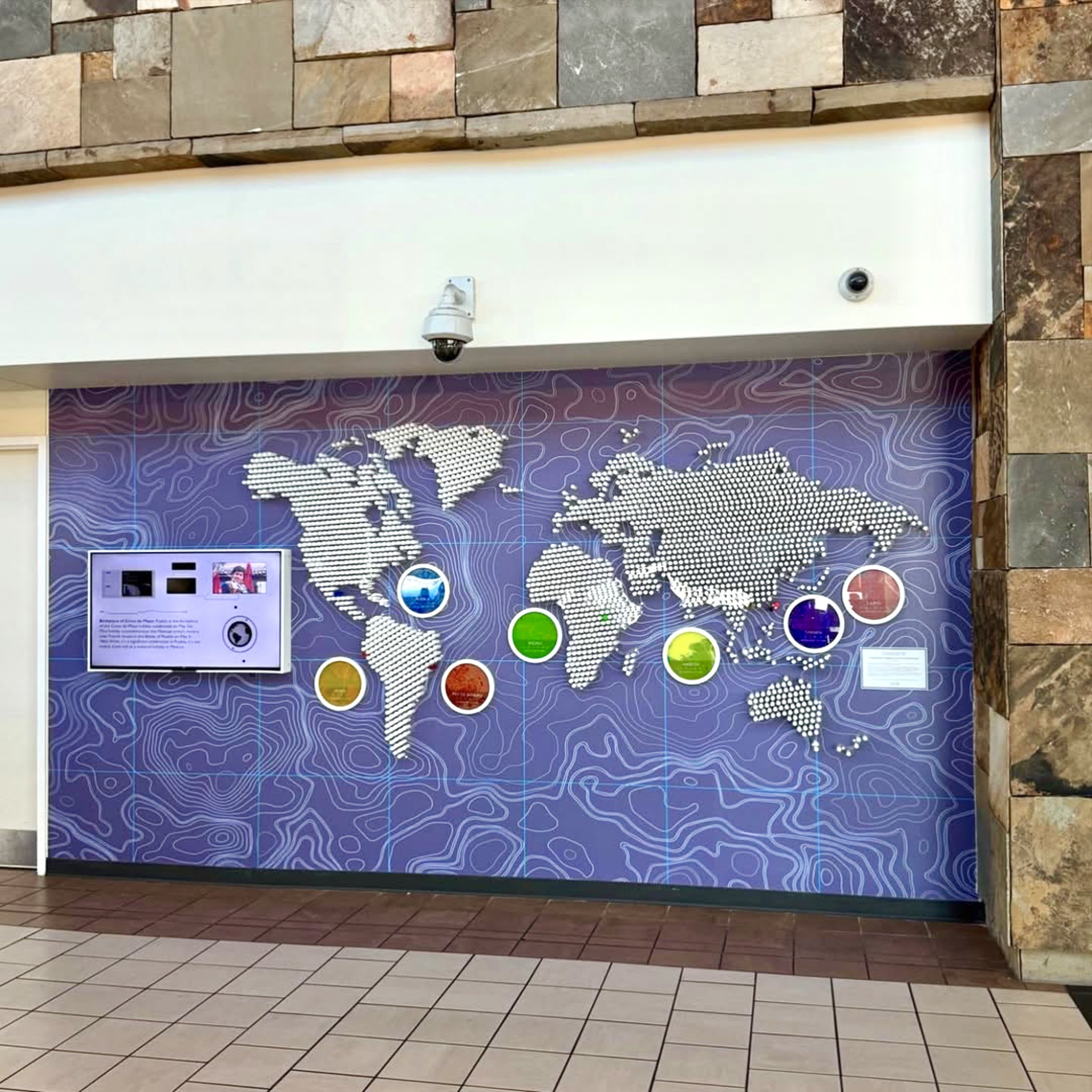Security camera mounted on a wall in front of purple display with white map outlines, brown brick tile outline wall, tiled floor.