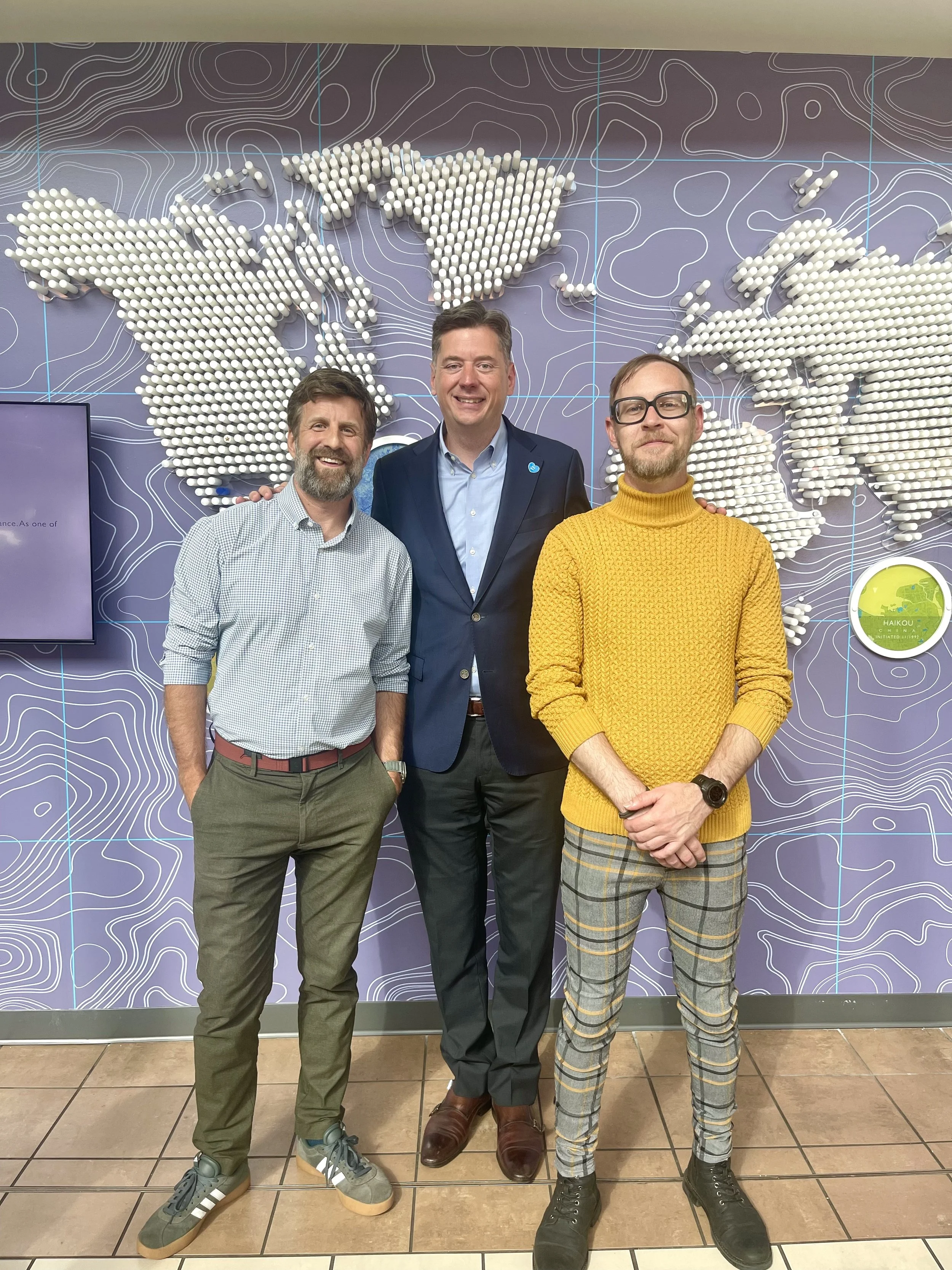 Kyle Van Osdol, Mayor David Holt, and Scott Henderson standing in front of a world map installation at the Will Rogers Airport in Oklahoma City.