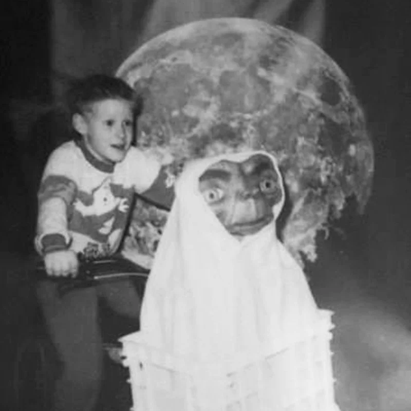 A young boy sitting next to a large puppet resembling Yoda, with a photo of the moon in the background.