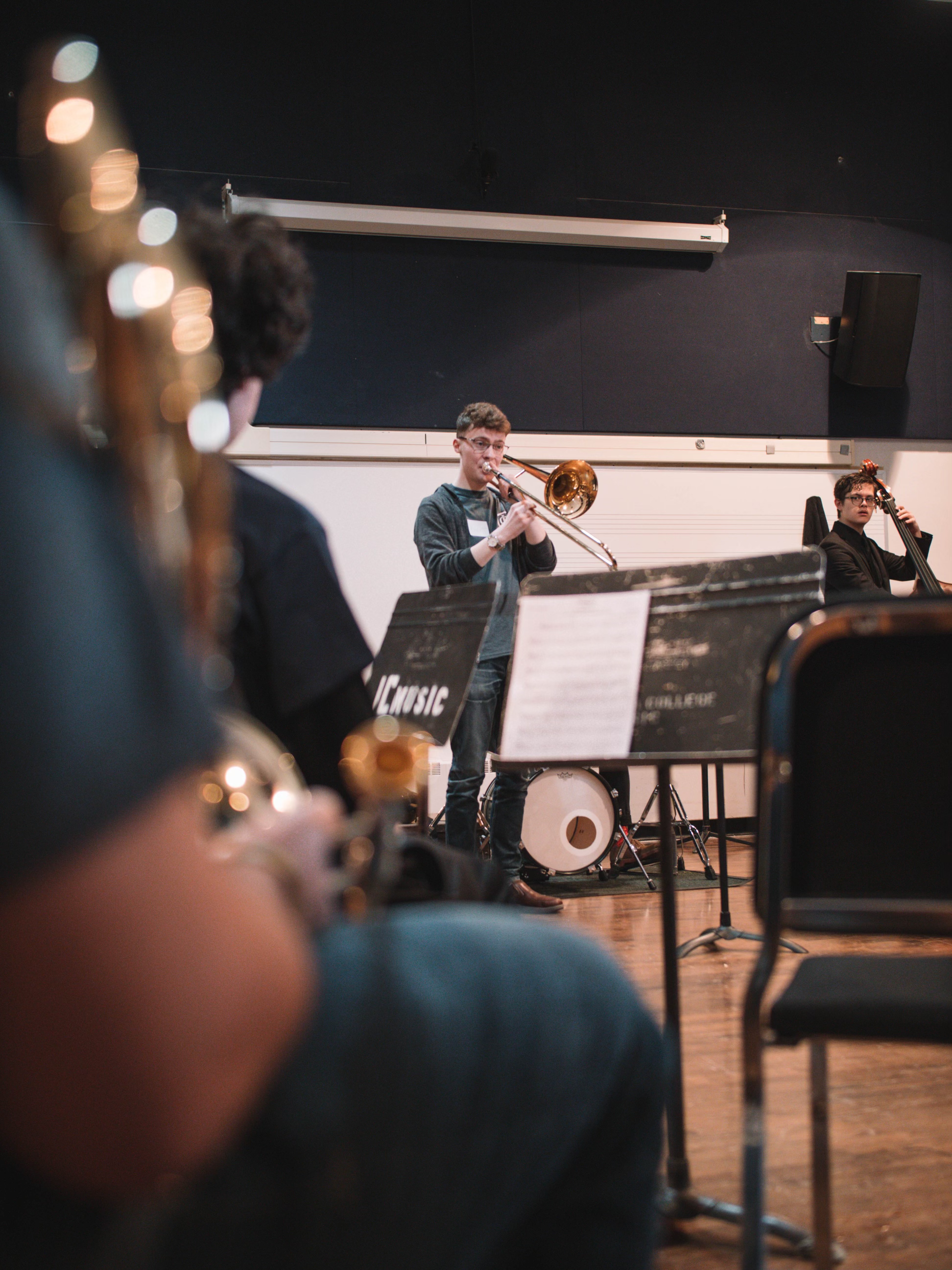 Musicians playing instruments during a rehearsal or performance in a music room with black walls and music stands.