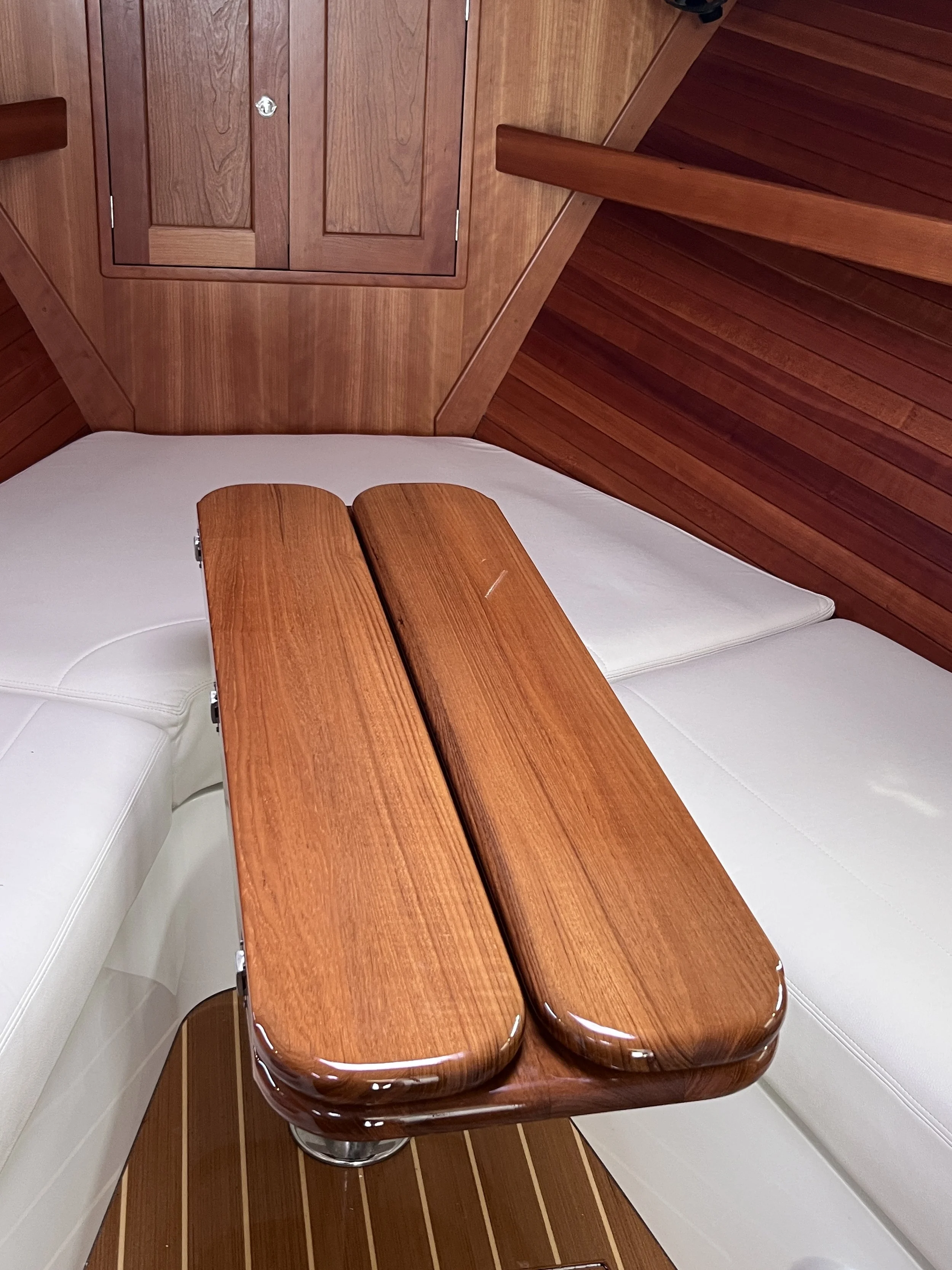 Interior of a boat with a wooden table, a white cushioned seat, wood-paneled walls, and horizontal wood planks on the ceiling.