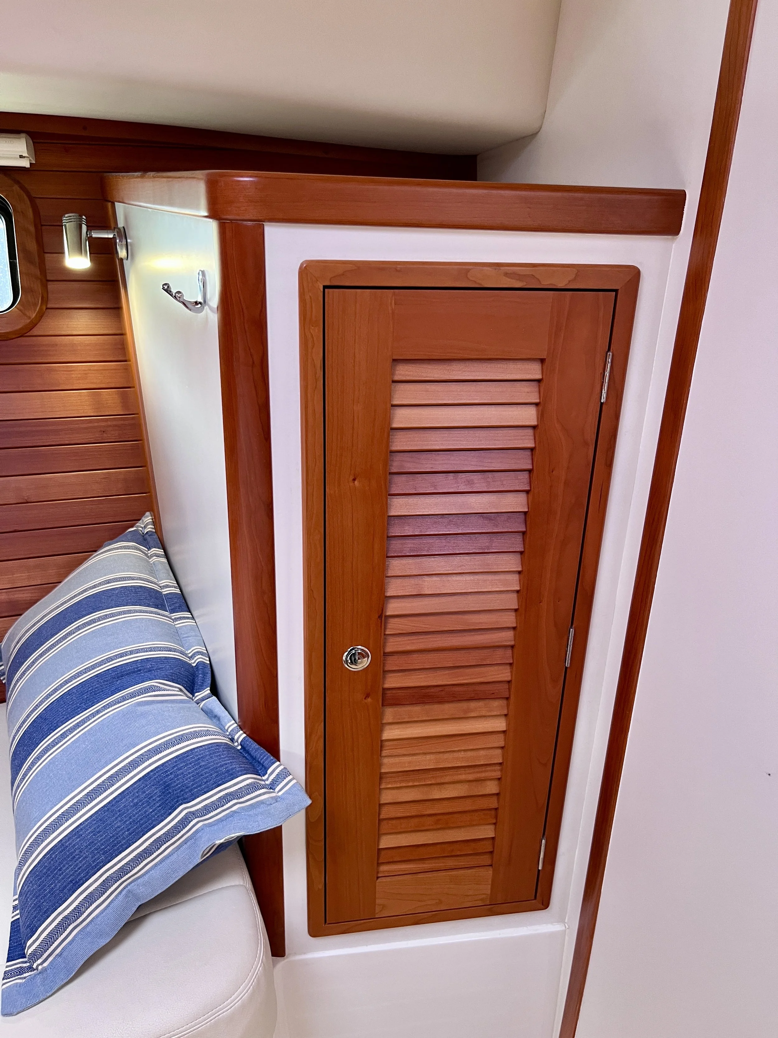 A small wooden cabinet with a louvered door next to a bed with striped blue and white bedding.