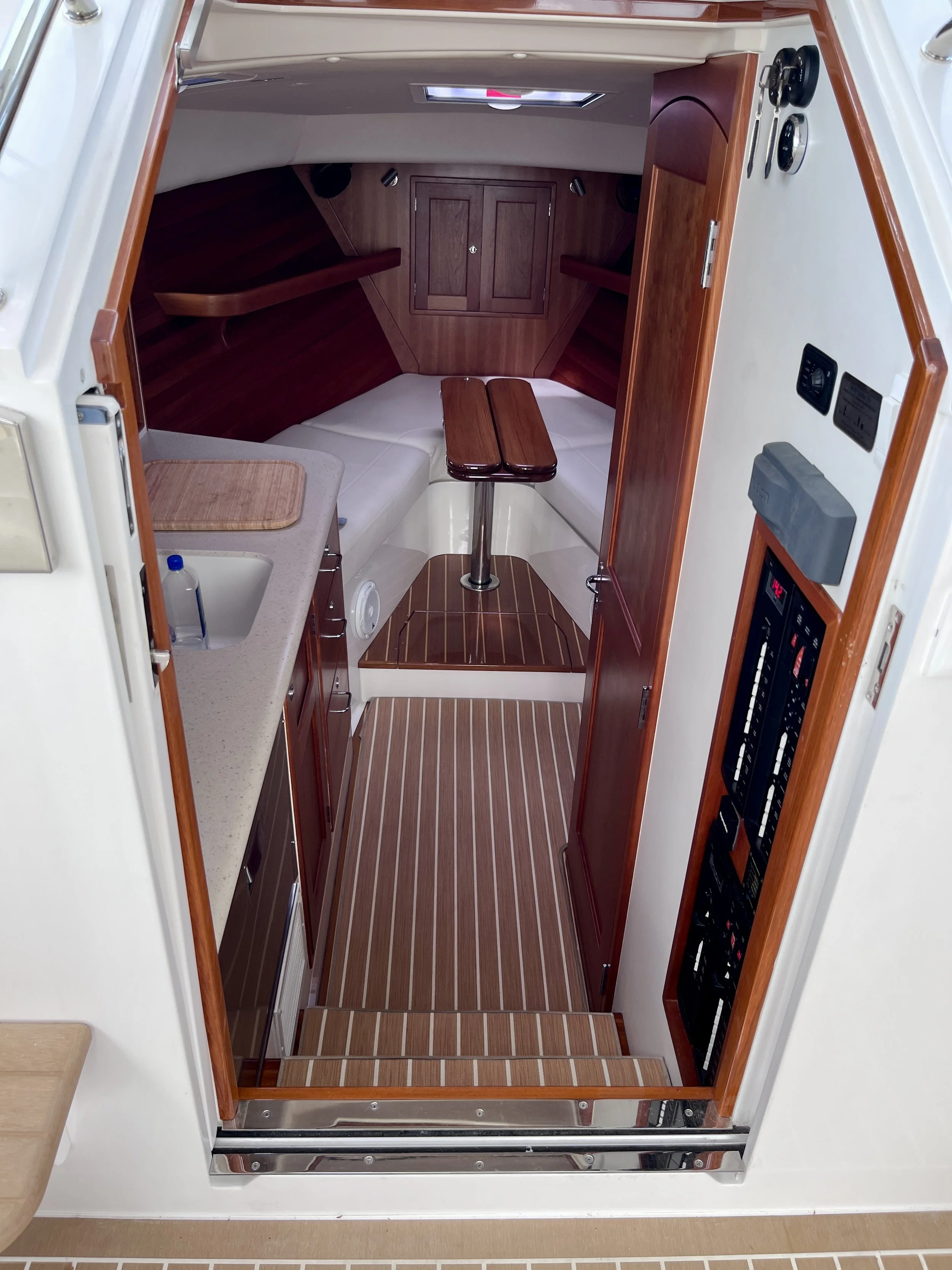 Interior view of a boat cabin with wooden ceiling and storage cabinet, white seating area, small table, and a countertop with a bottle.
