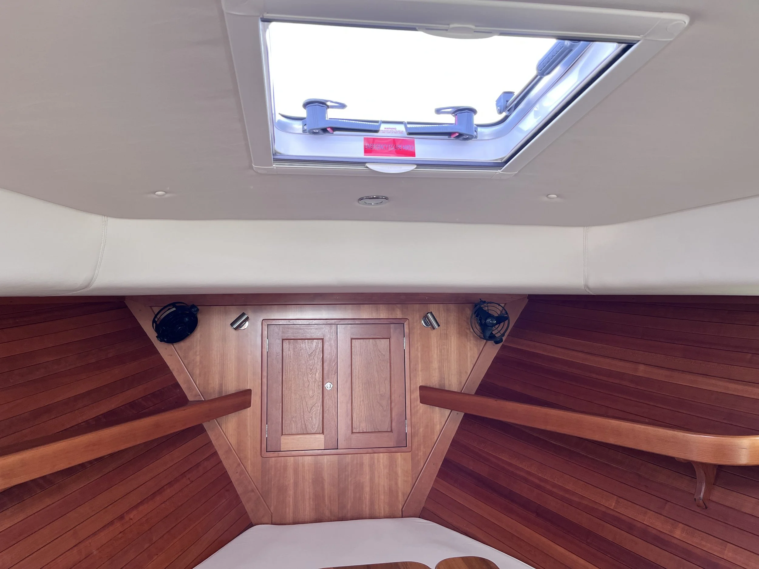 View of boat ceiling and interior with wooden panels, an open skylight, and a small roof hatch, with two fans and some objects on wooden floor.