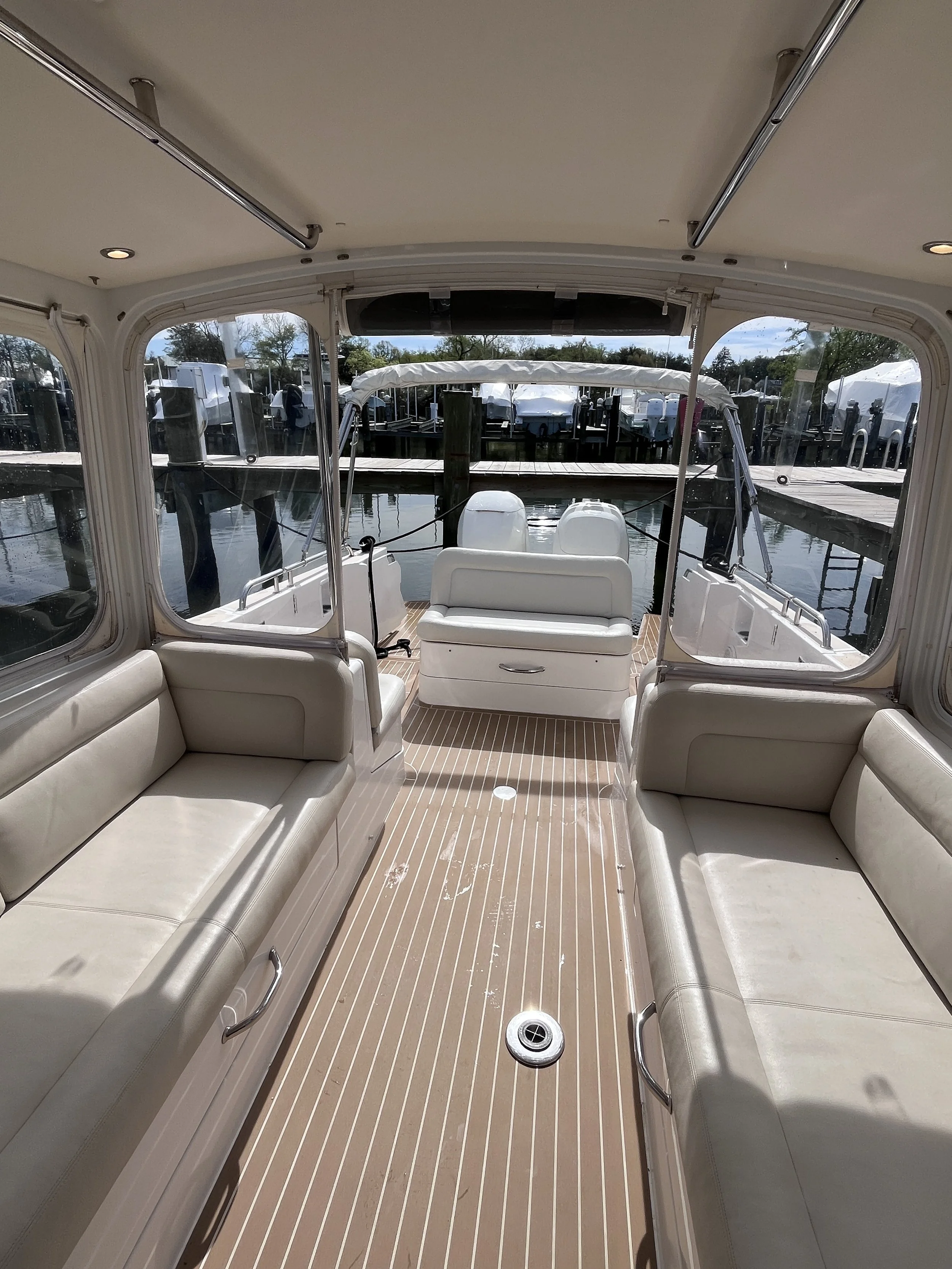 View from the entrance of a boat showing white seating on both sides, a center table, and a view of the dock and water outside.